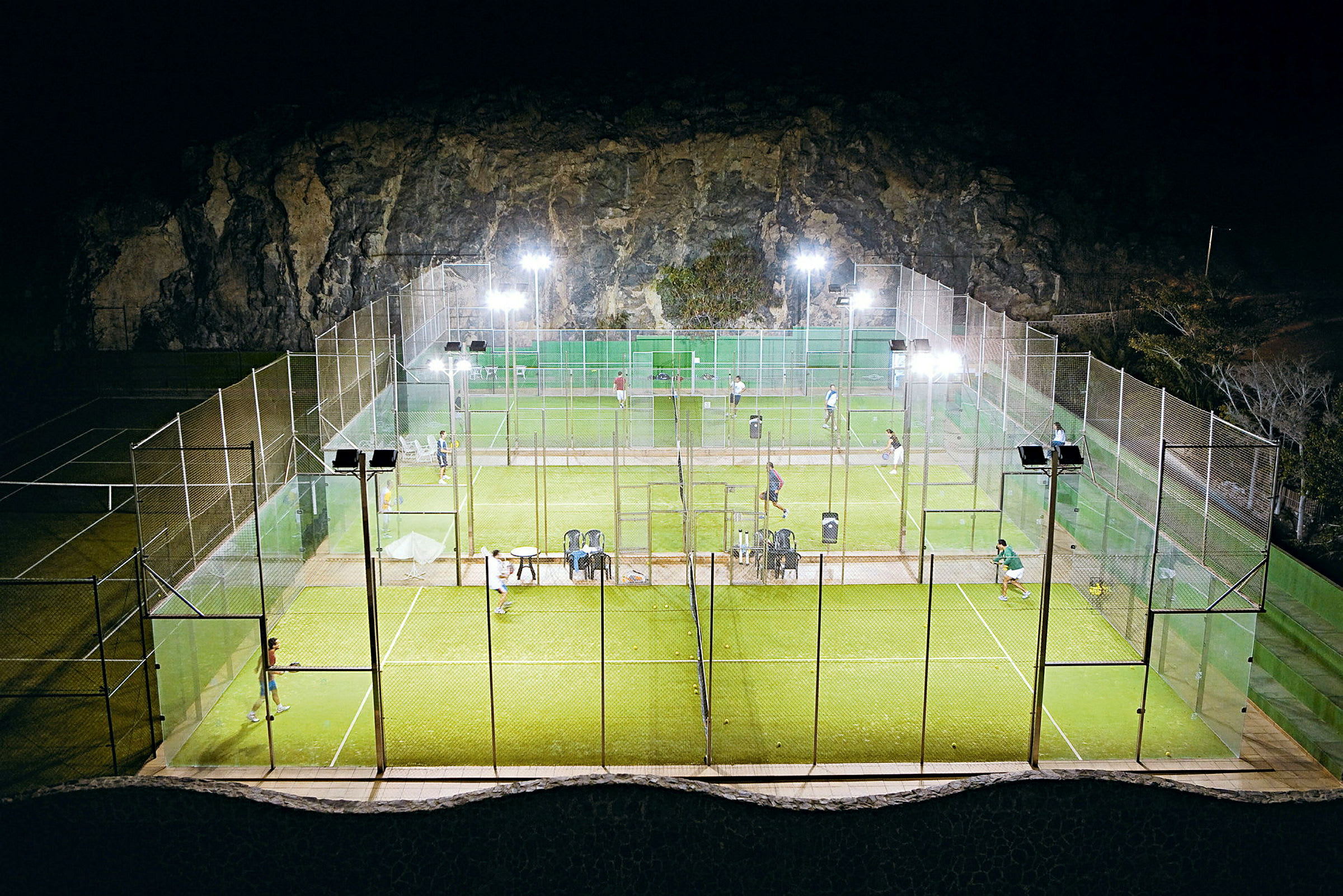 Padelbanor utomhus belysta på kvällen, spelare synliga på banan. (AI-genererad text)