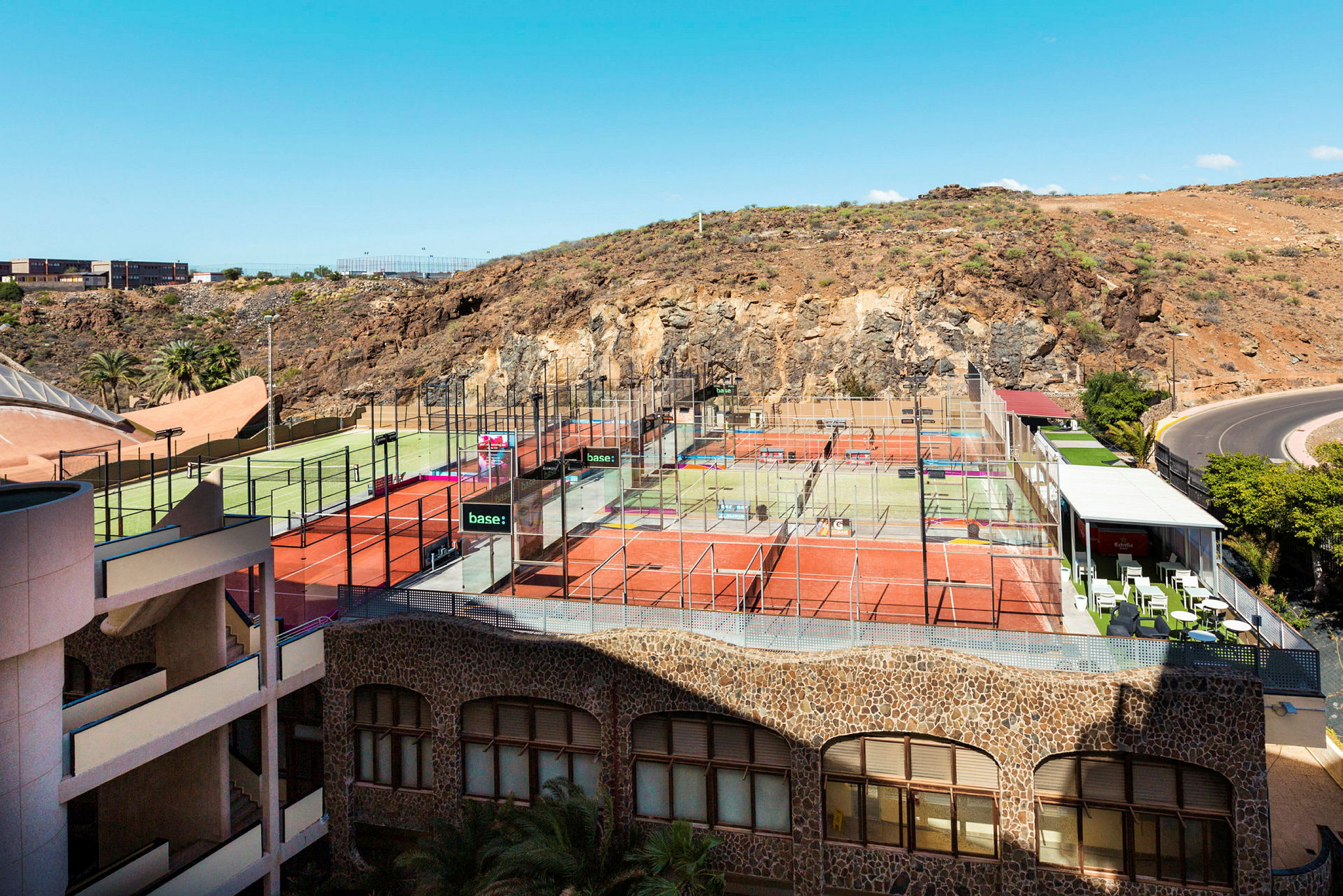 Sportanläggning med flera racketbanor vid berg och klar himmel. (AI-genererad text)