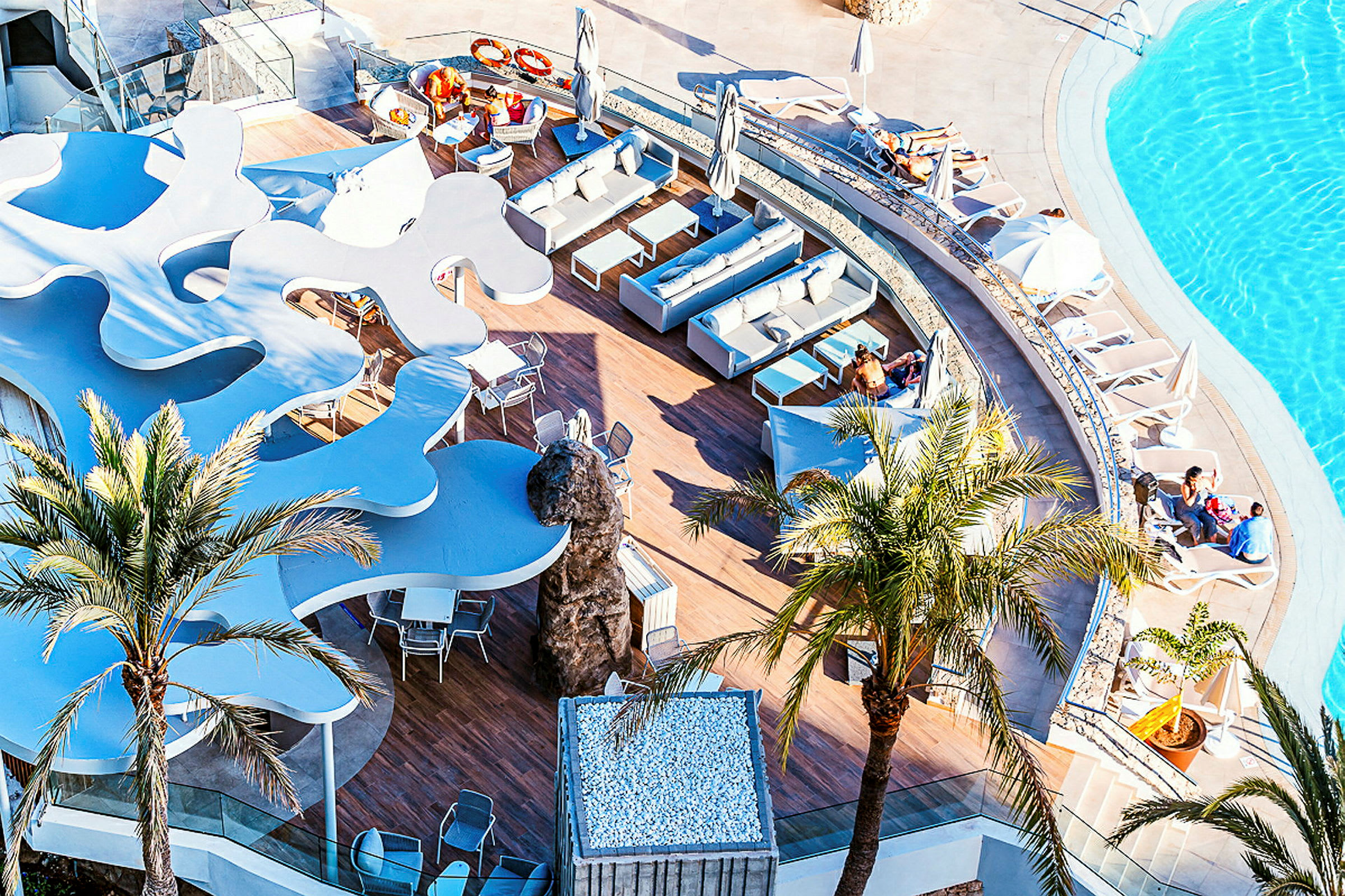 Utsikt över en pool och en terrass med sittgrupper och solstolar. (AI-genererad text)
