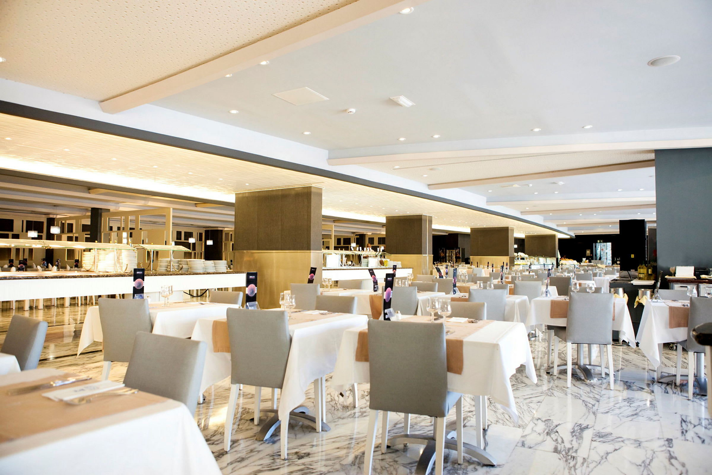 En rymlig restaurang med elegant uppsatta bord, vita dukar och grå stolar. (AI-genererad text)