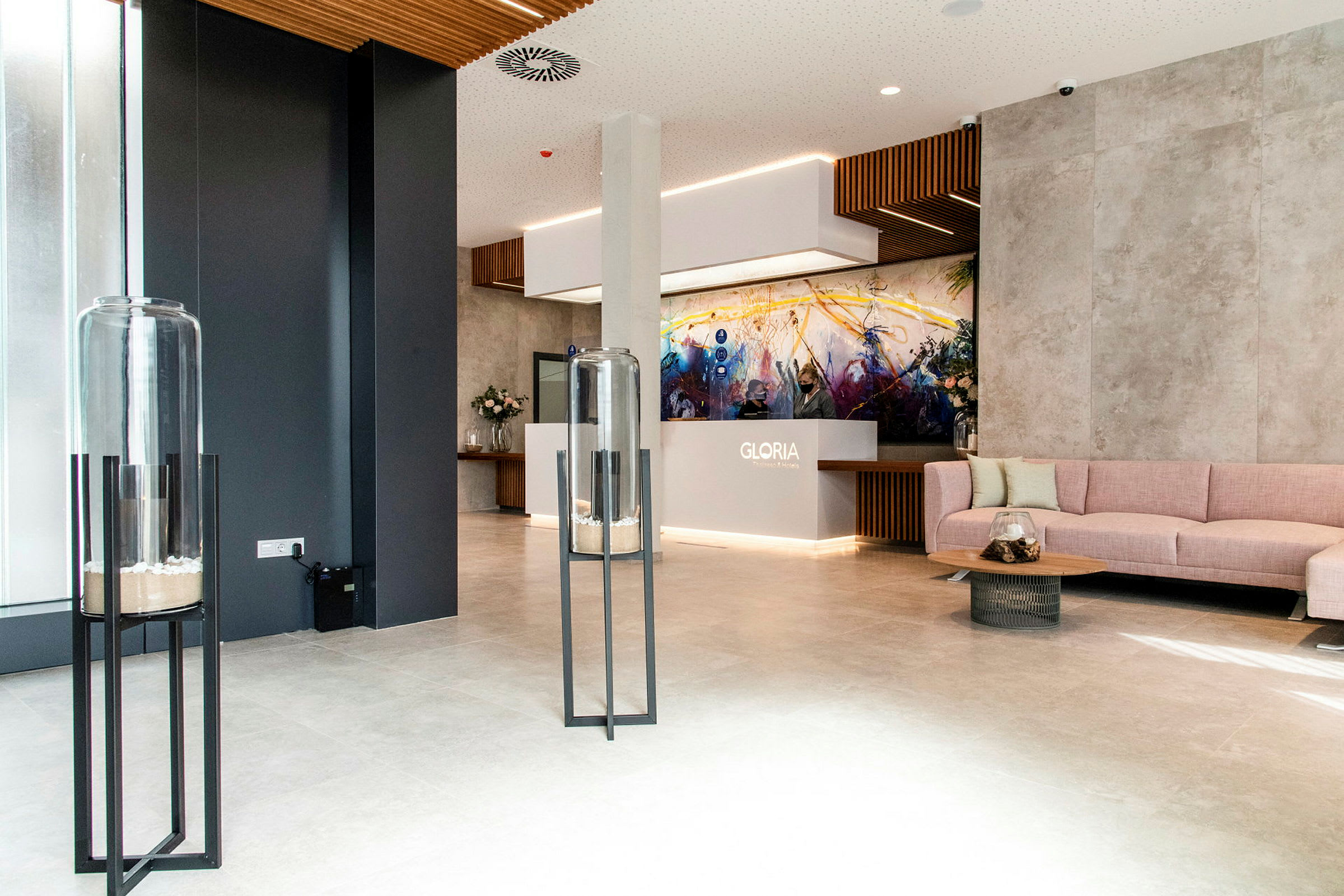 Modernt hotellobby med receptionen märkt ‘Gloria’, sittmöbler och dekorativa element såsom glasbehållare på stativ. (AI-genererad text)