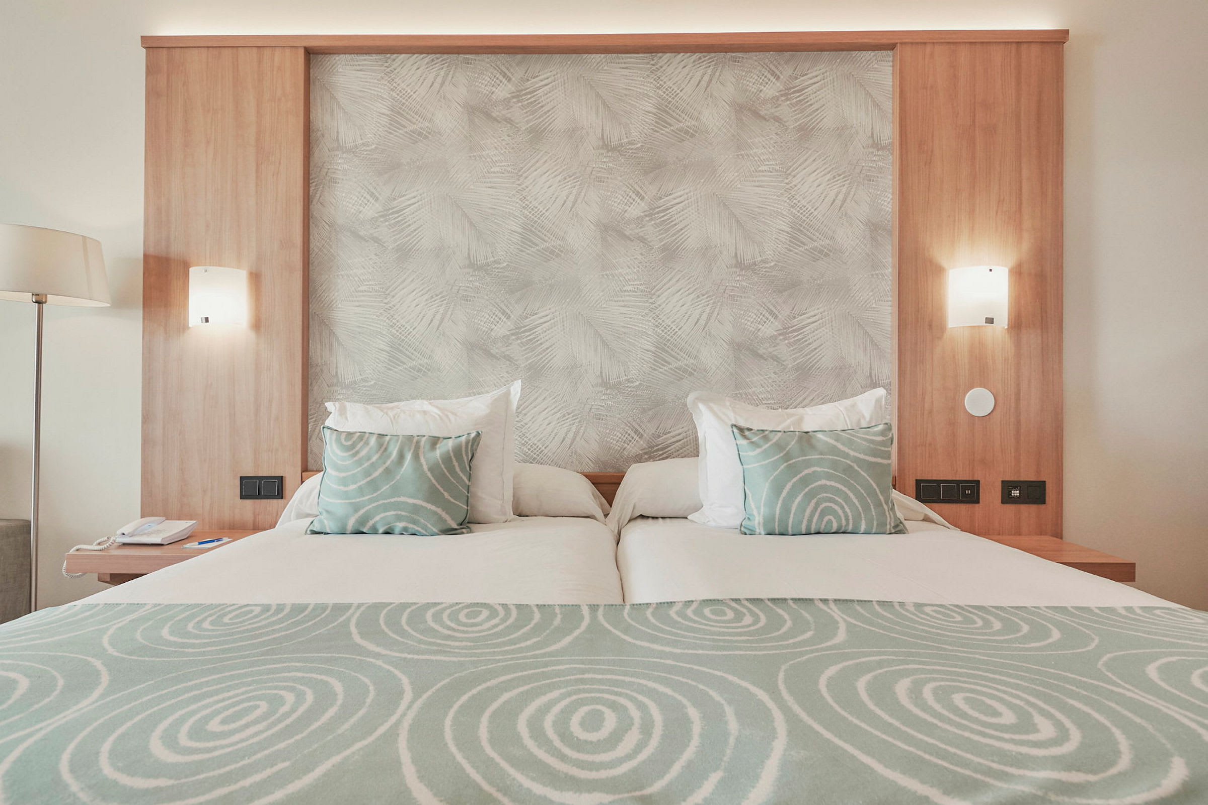 Hotellsäng med ljust träpanel, gröna cirkelmönstrade kuddar och matchande sängklädsel. (AI-genererad text)