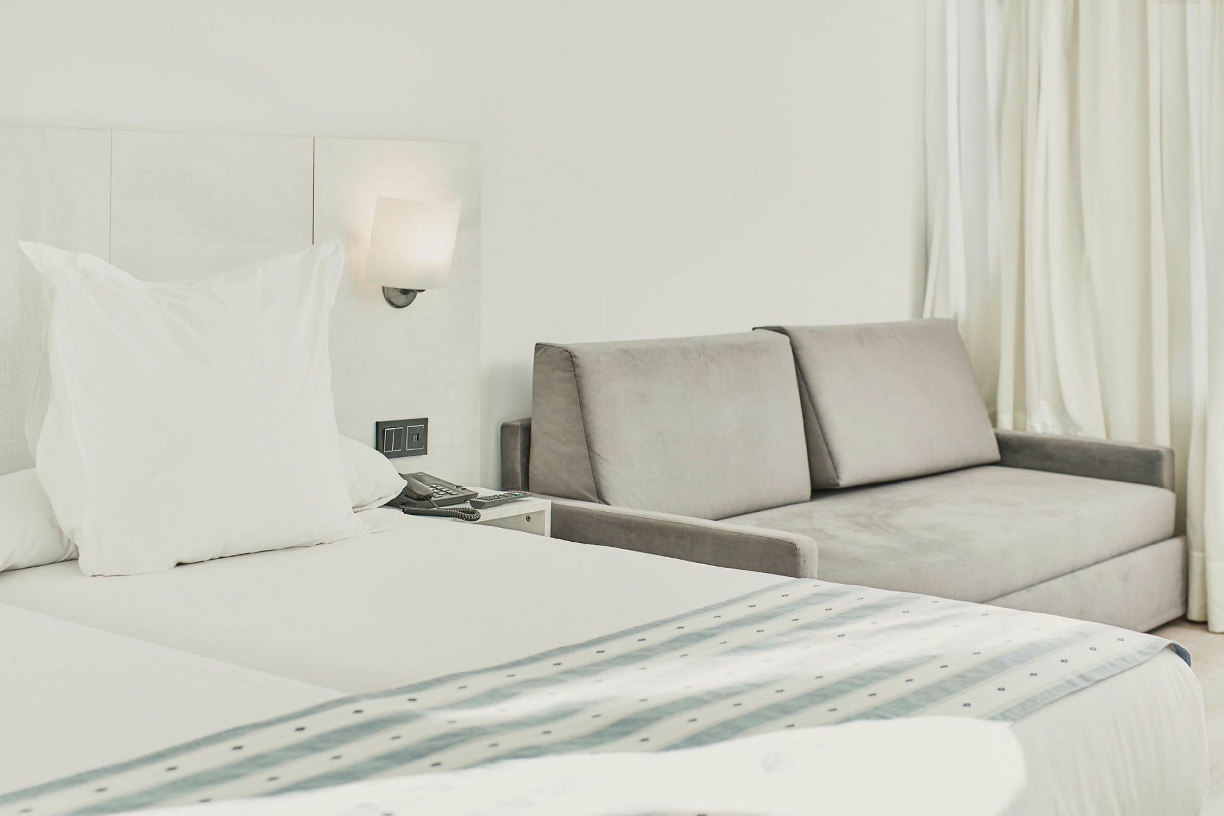 Hotelrum med säng och grå soffa vid sidan. (AI-genererad text)
