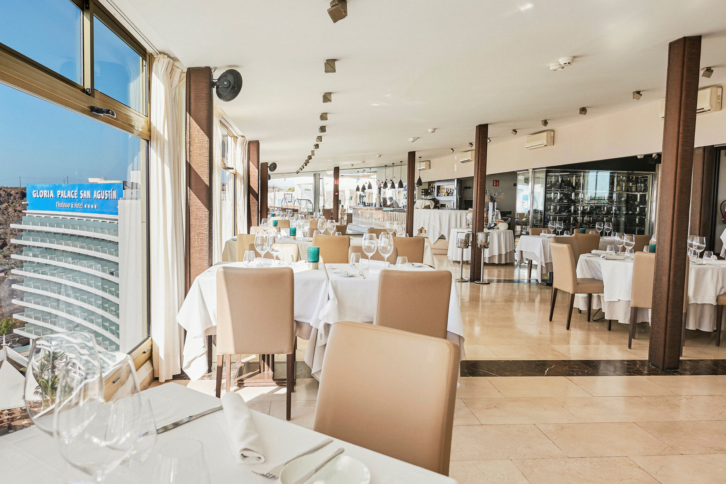 Bild på en restaurang med dukade bord och stolar bredvid stora fönster. (AI-genererad text)