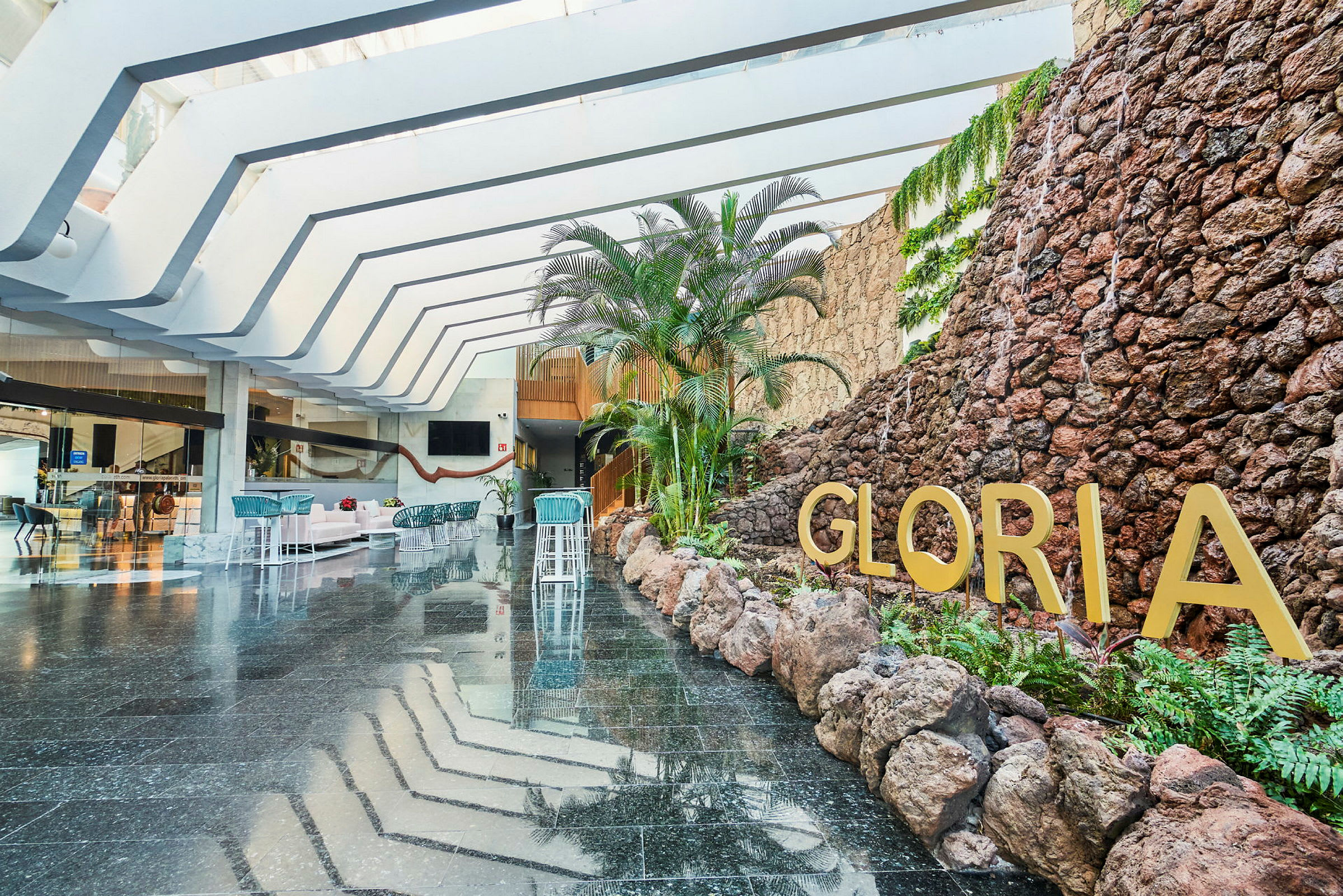 Hotellobby med stenvägg, växter och texten Gloria. (AI-genererad text)