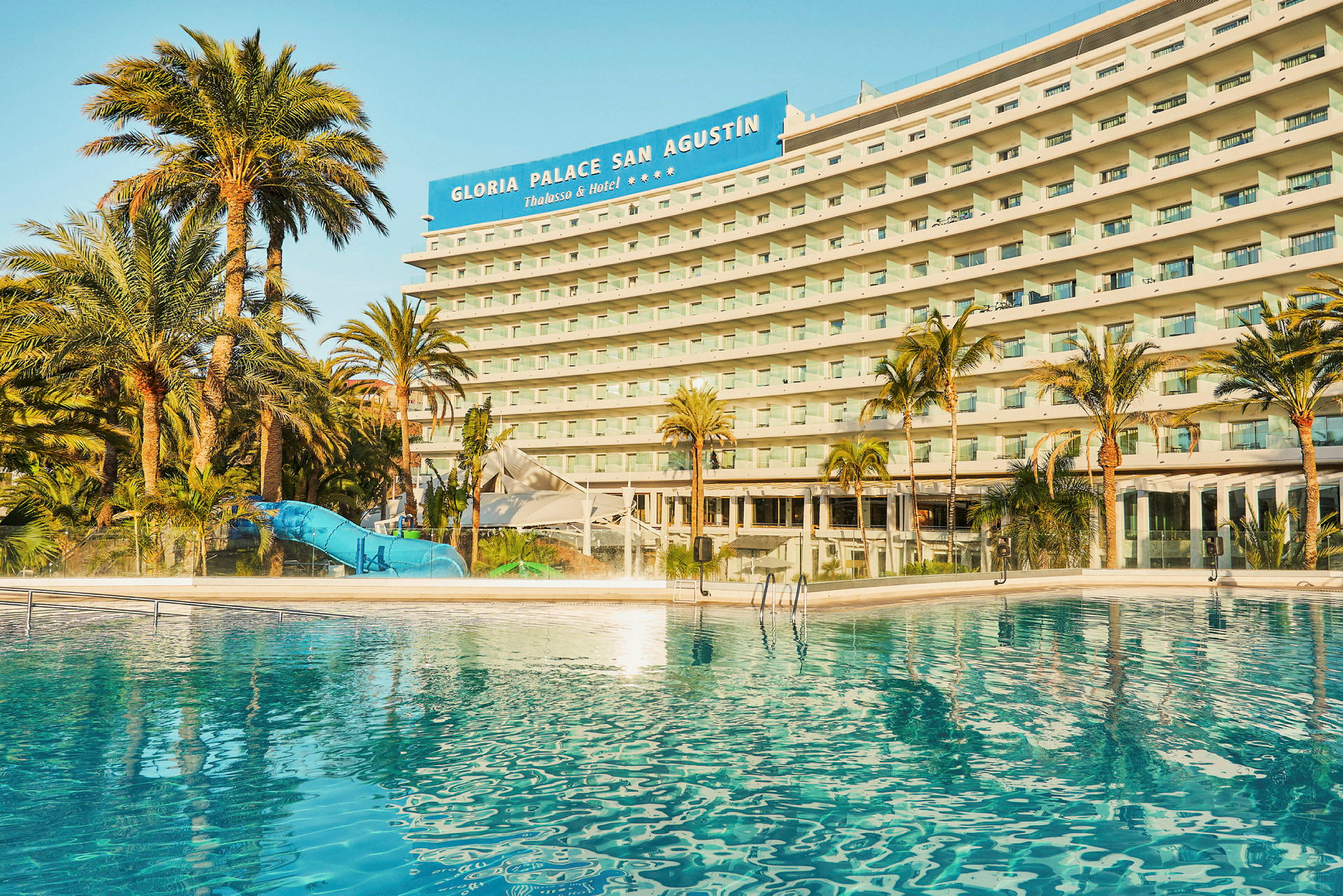 Ett hotell med en pool och palmer i förgrunden. (AI-genererad text)