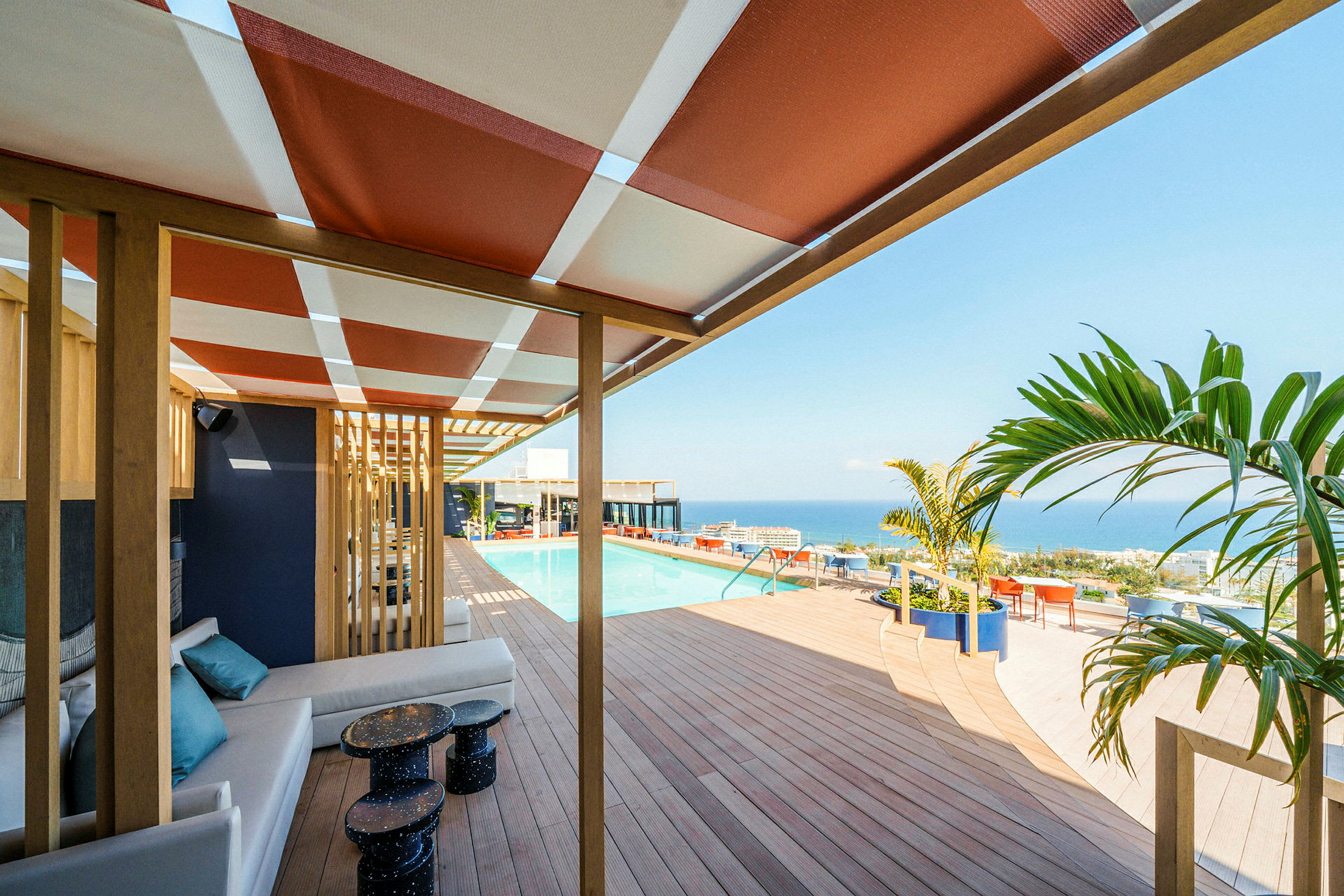 En terrass med skugga av tak och sittplatser med utsikt över en pool och havet. (AI-genererad text)