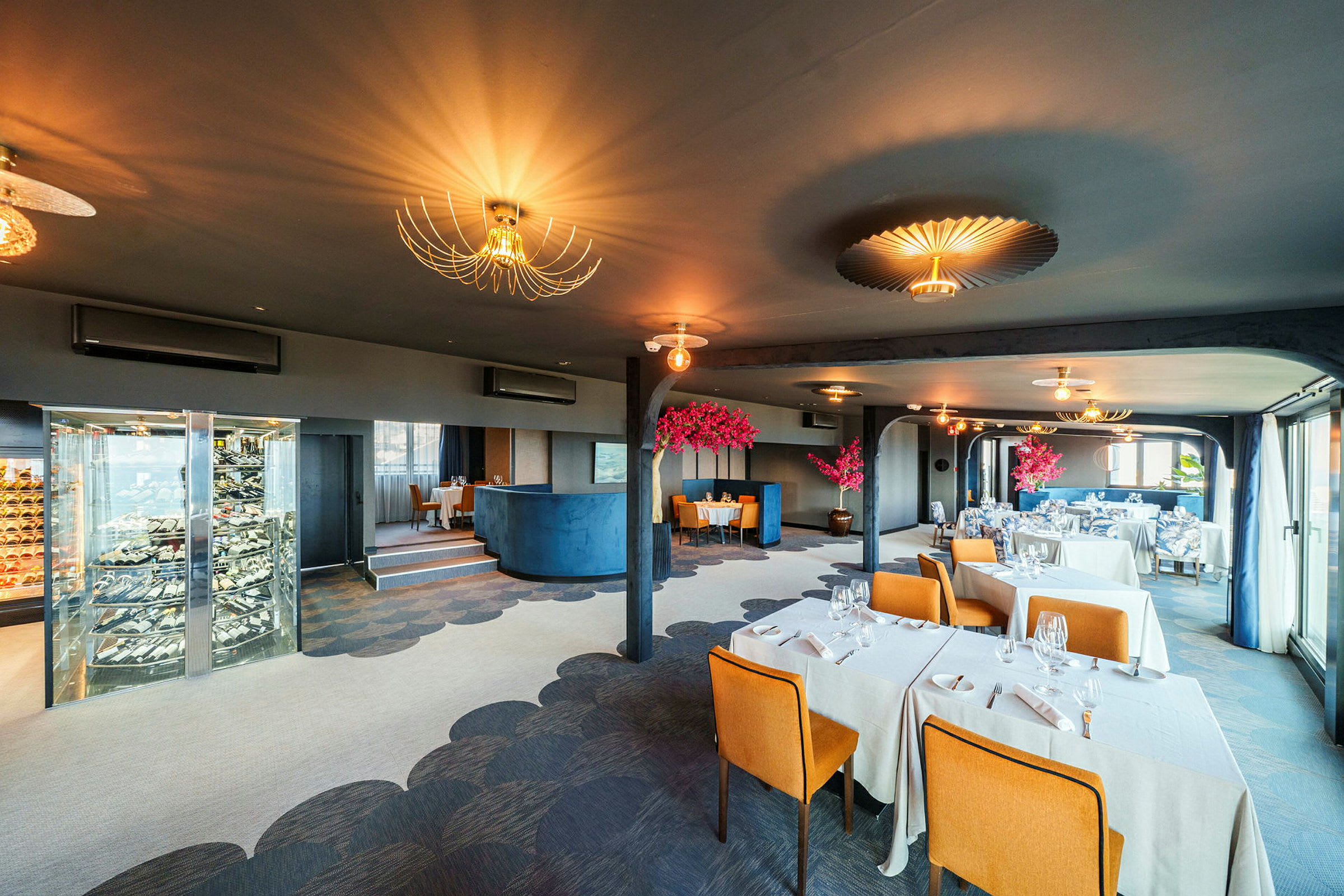En elegant restaurang med dukade bord, guldfärgade taklampor och dekorativa rosa träd. (AI-genererad text)