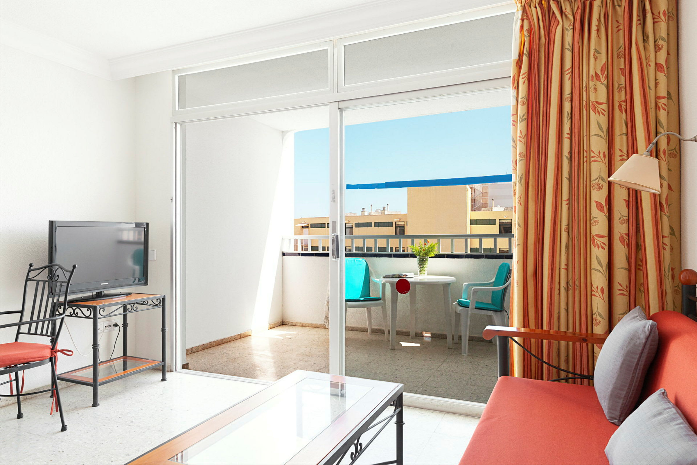 Ett hotellrum med en soffa, en TV och ett bord, samt en balkong med sittmöbler. (AI-genererad text)