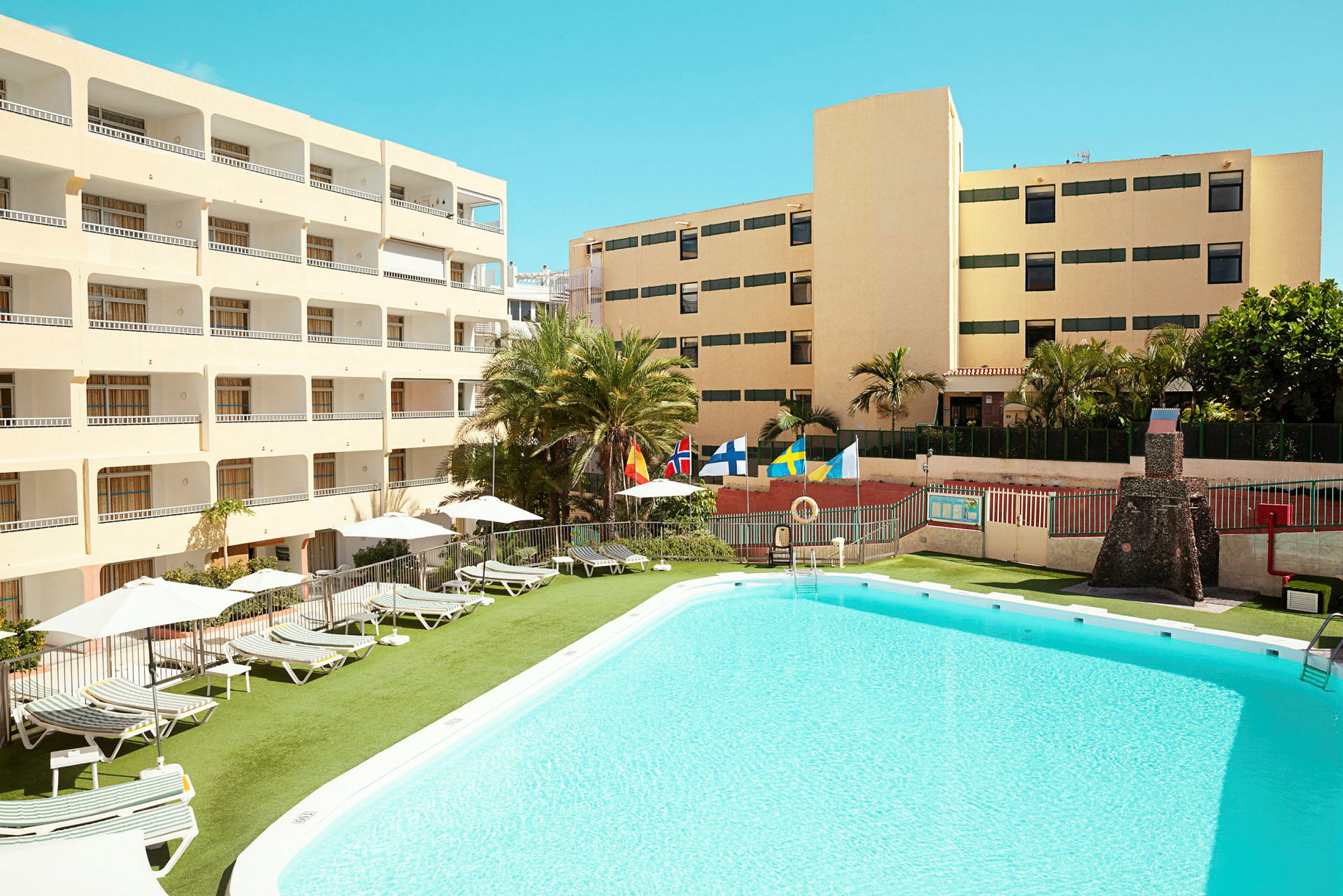 En bild av ett hotellområde med pool och solstolar. Byggnader omger området. (AI-genererad text)