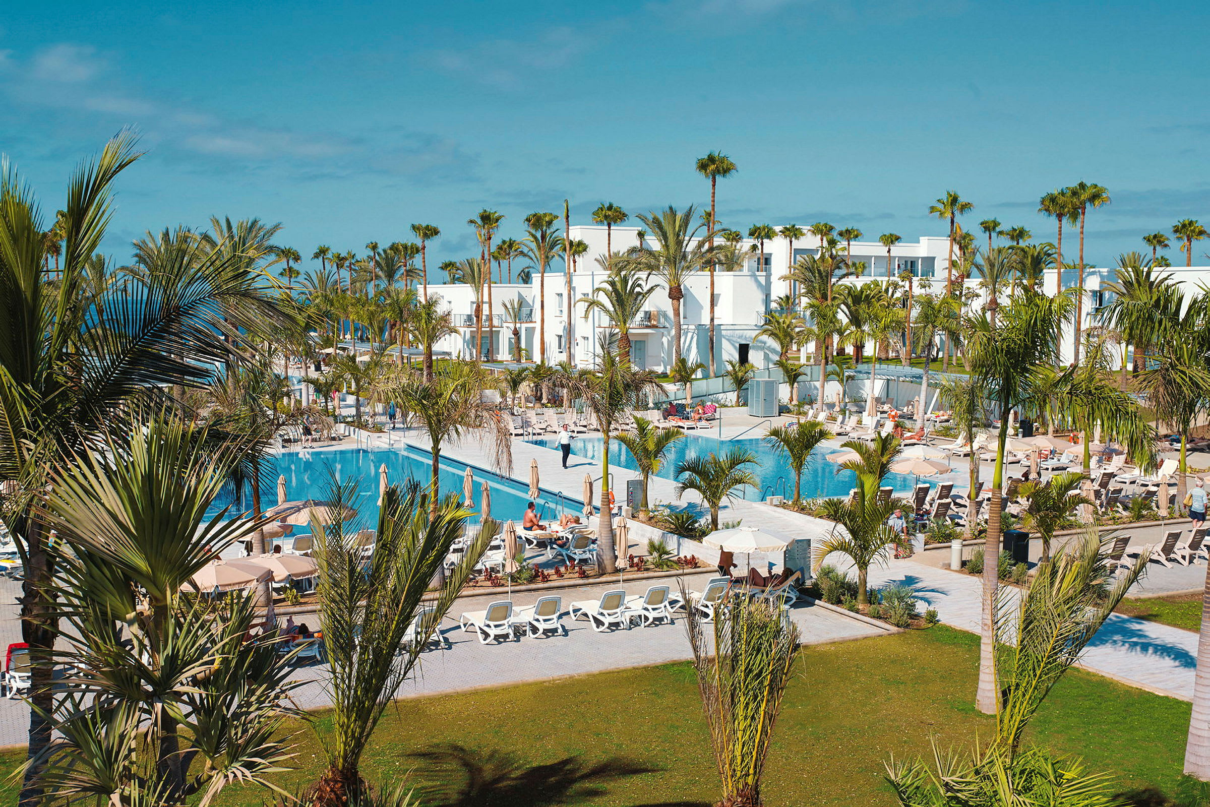 Hotellområde med vita byggnader, swimmingpooler och palmer. (AI-genererad text)