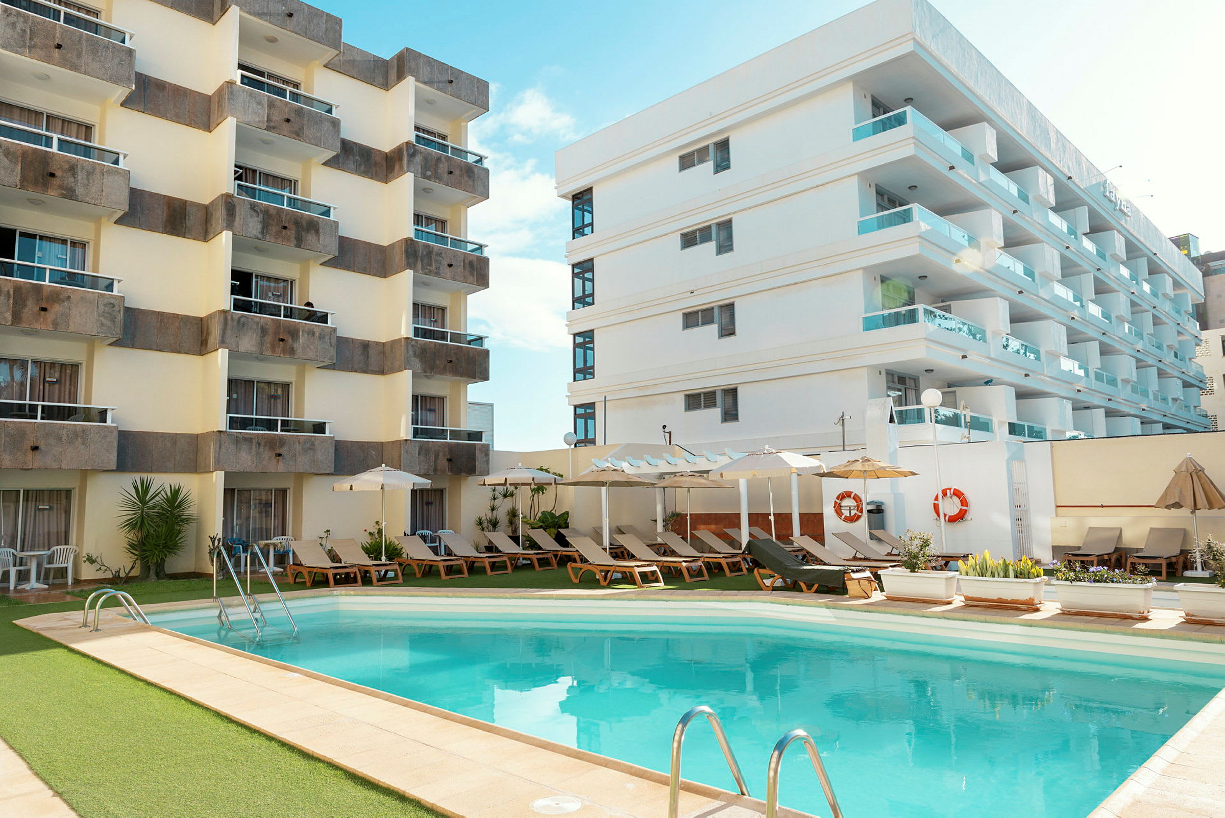 Hotellbyggnader vid en utomhuspool omgivna av solstolar och parasoller. (AI-genererad text)