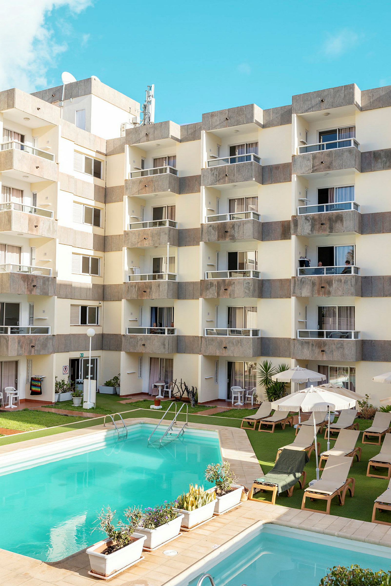 Bild av ett hotell med en pool framför och solstolar med parasoller. (AI-genererad text)