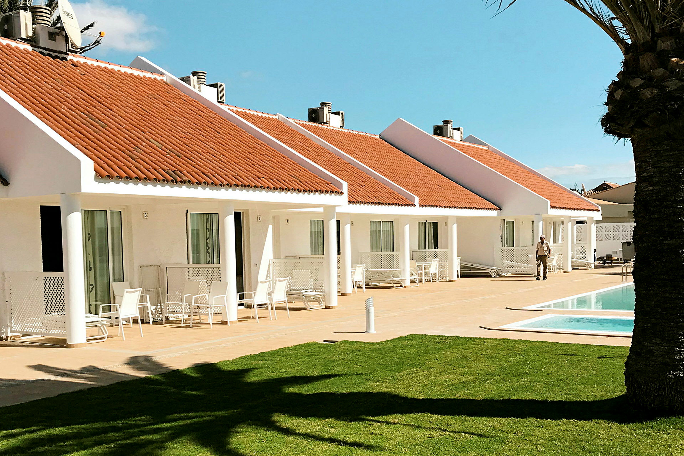 Vita bungalows med orangea tak och en pool framför. En gräsmatta i förgrunden. (AI-genererad text)