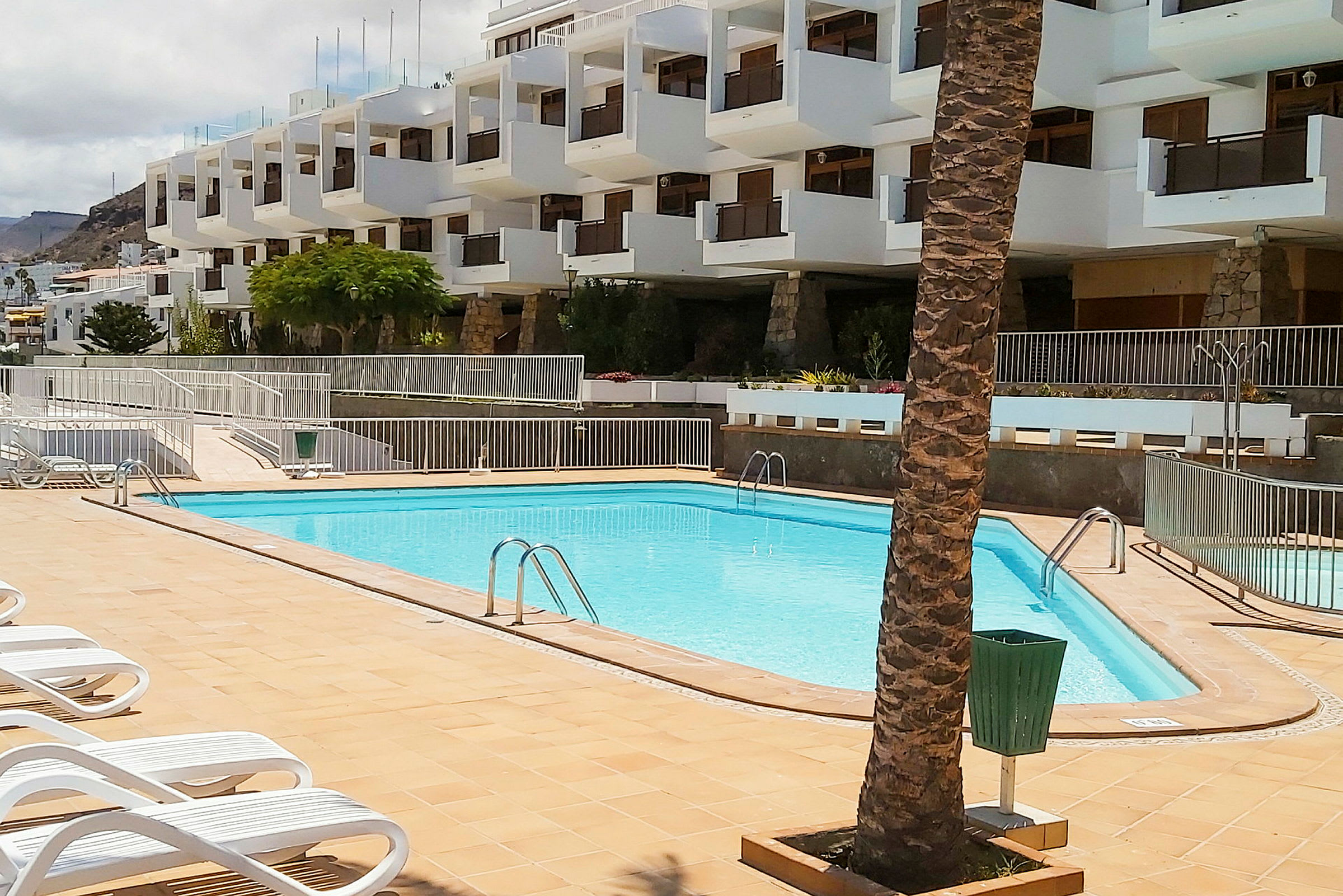Pool med solsängar framför en vit byggnad. (AI-genererad text)