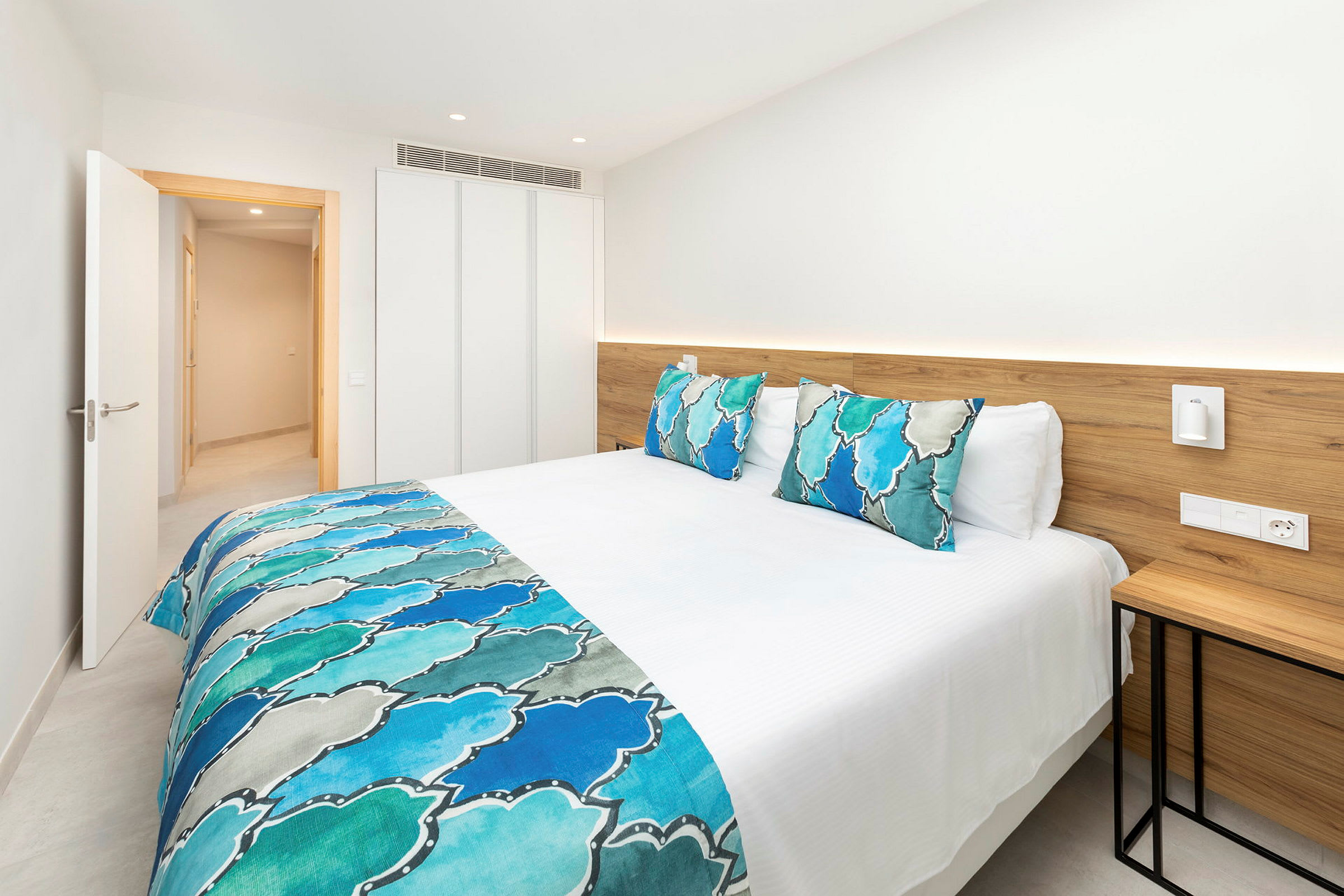 Säng med vita sängkläder och blå dekorativa detaljer i ett ljust hotellrum. (AI-genererad text)