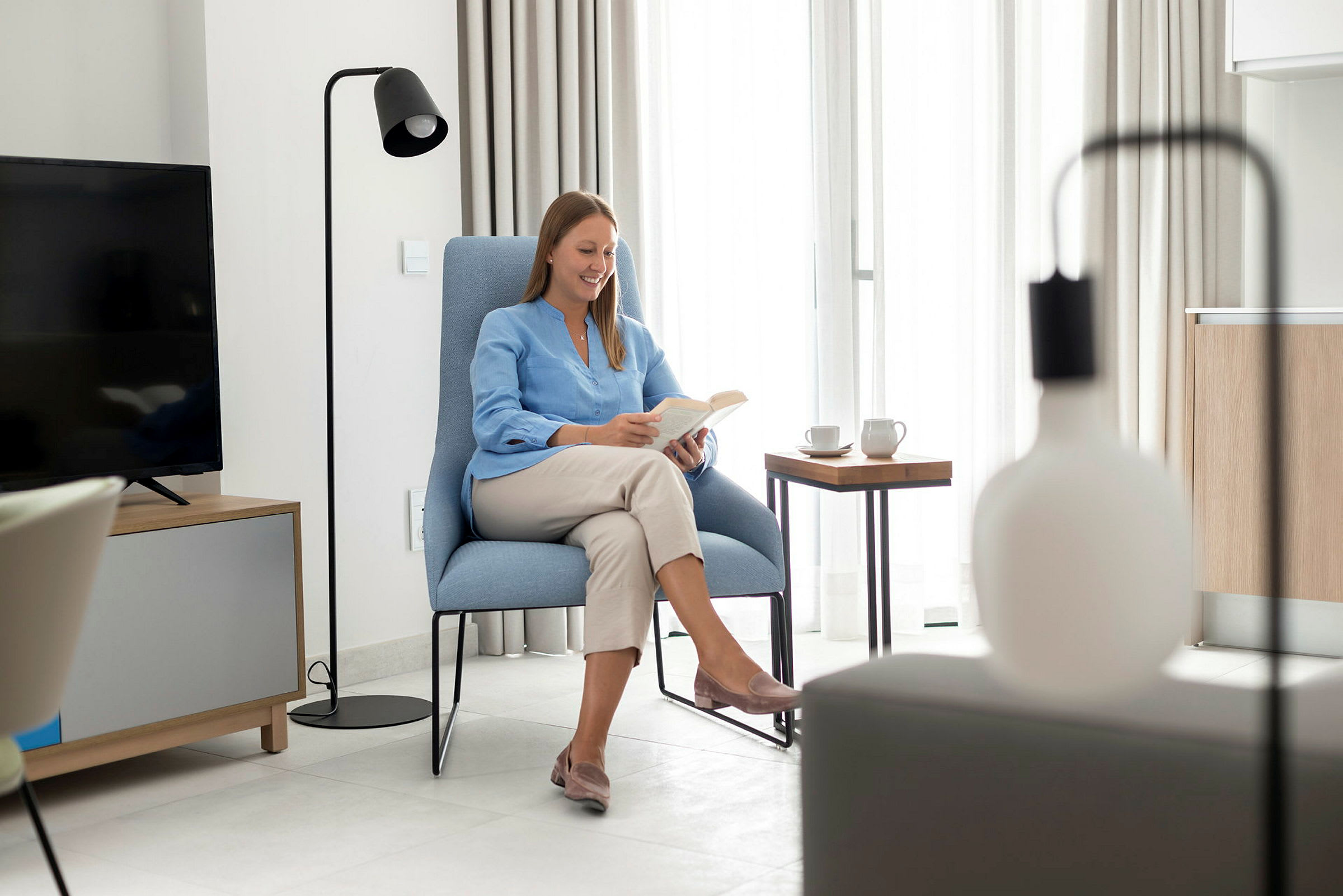 Modern inredning med en person som sitter och läser i en solbelyst vardagsrumsmiljö. (AI-genererad text)