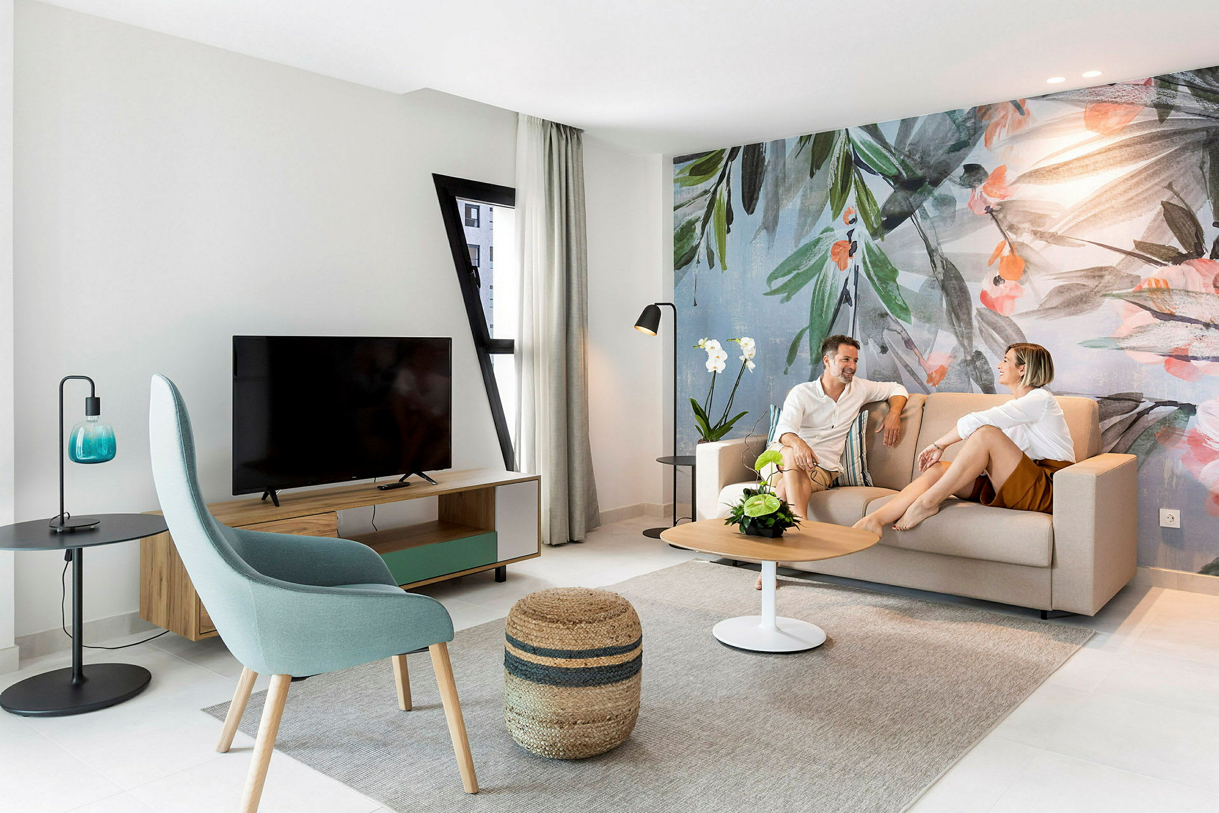 Ett modernt vardagsrum med en soffa, bord och väggdekoration med botaniskt tema. (AI-genererad text)