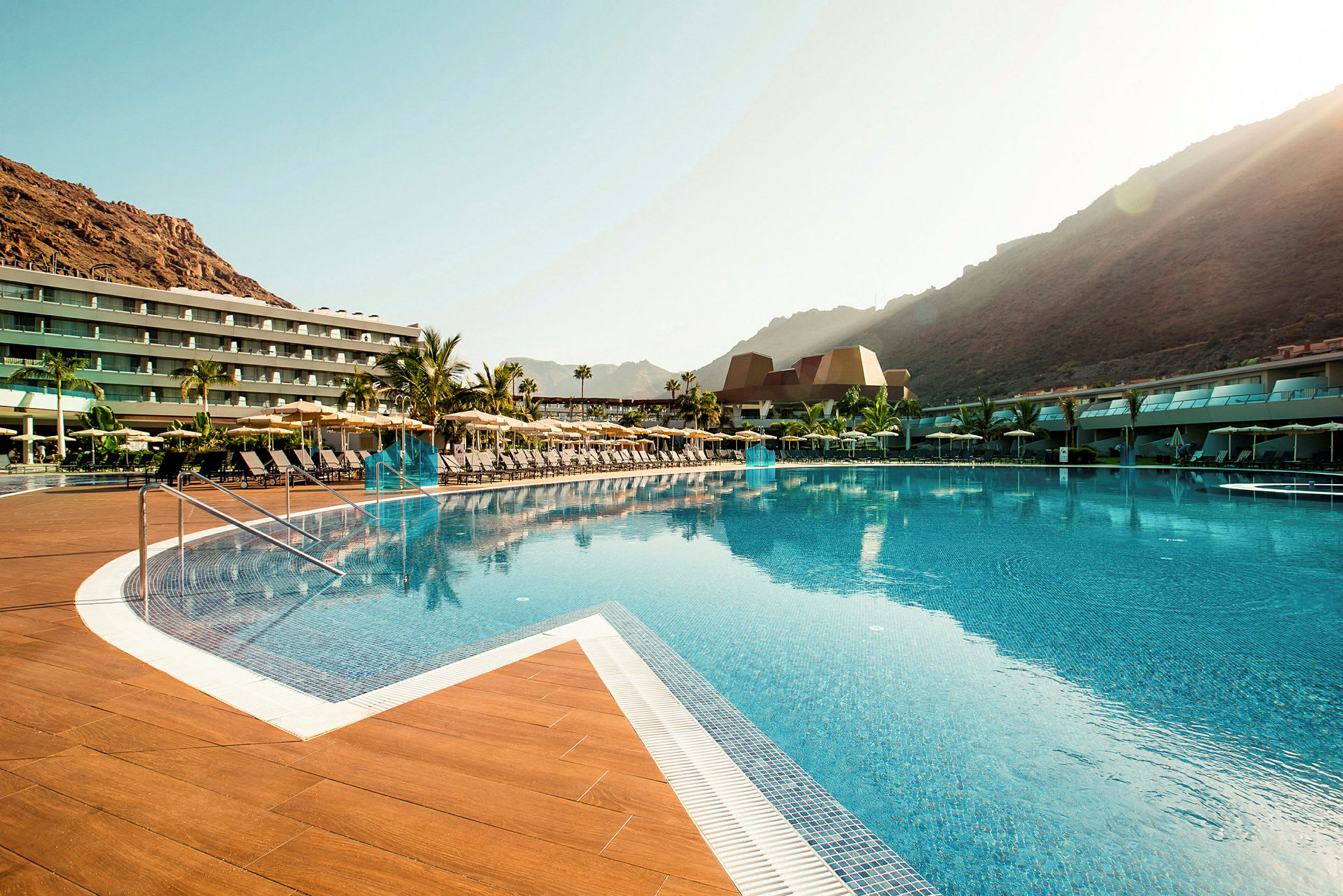 Stor pool med solstolar och ett hotell i bakgrunden. (AI-genererad text)