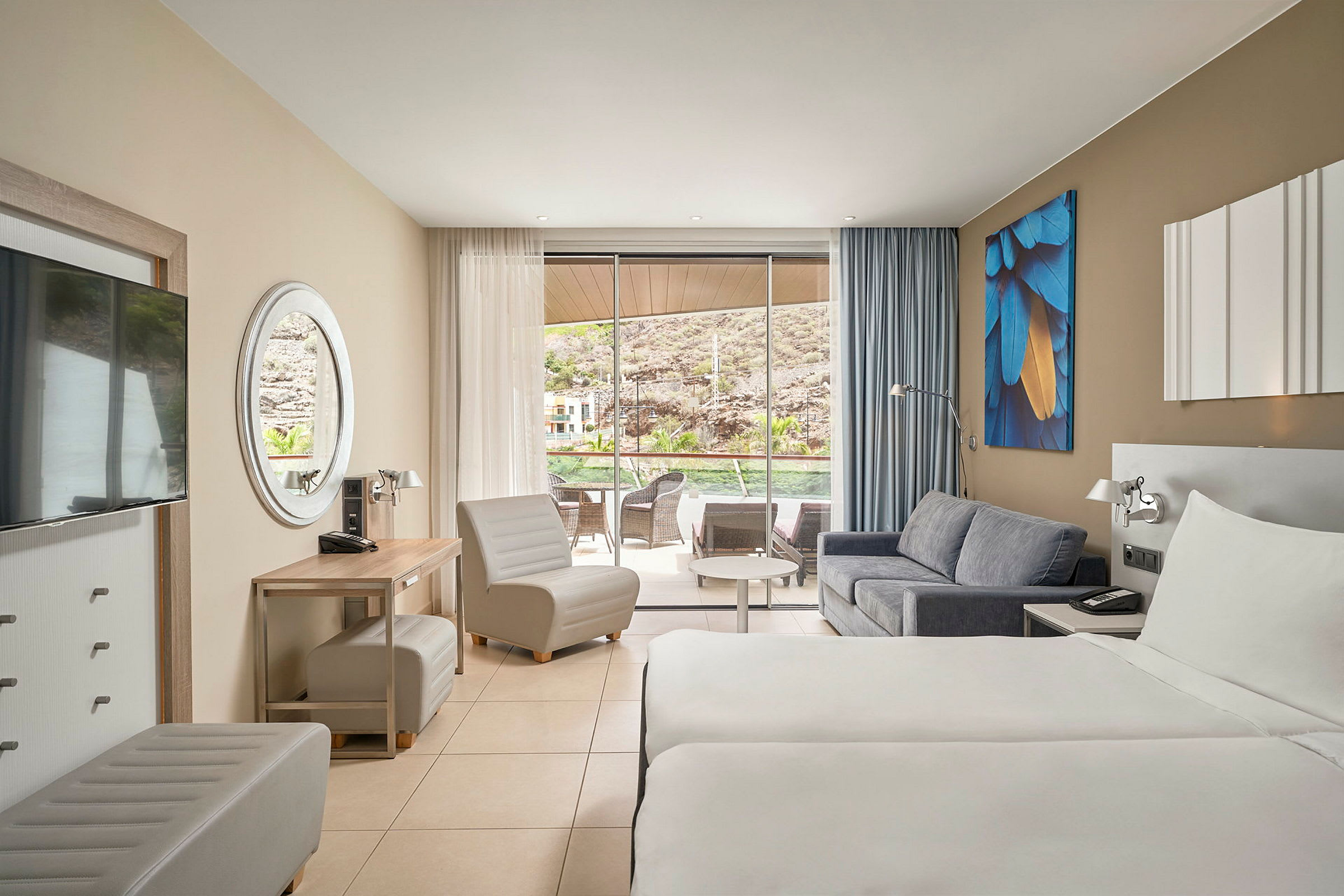 Hotelrum med två enkelsängar, soffa och sittmöbler. Glasdörrar leder till en terrass med utsikt. (AI-genererad text)
