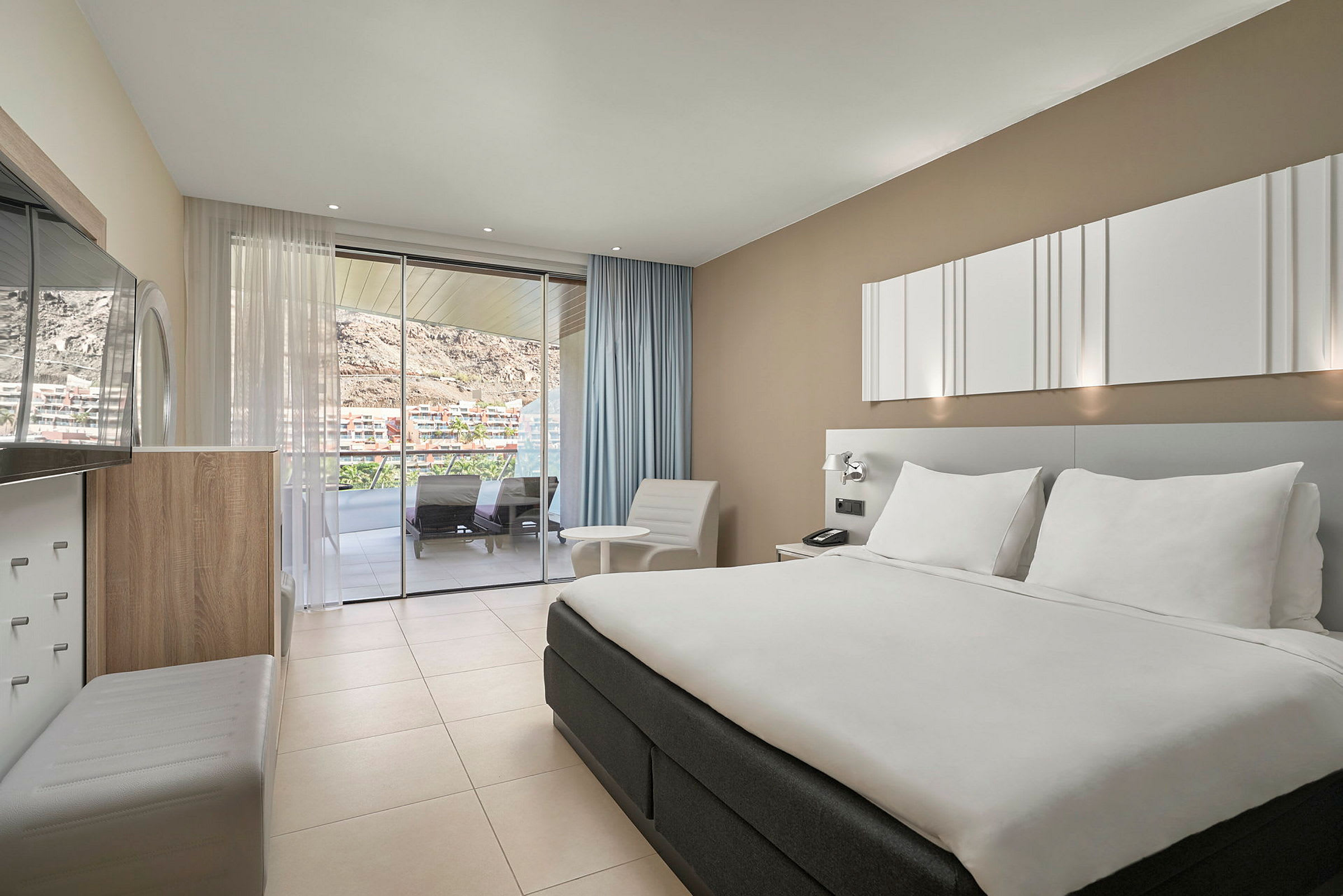 Hotellrum med stor säng, sittmöbler, och utsikt från balkong. (AI-genererad text)