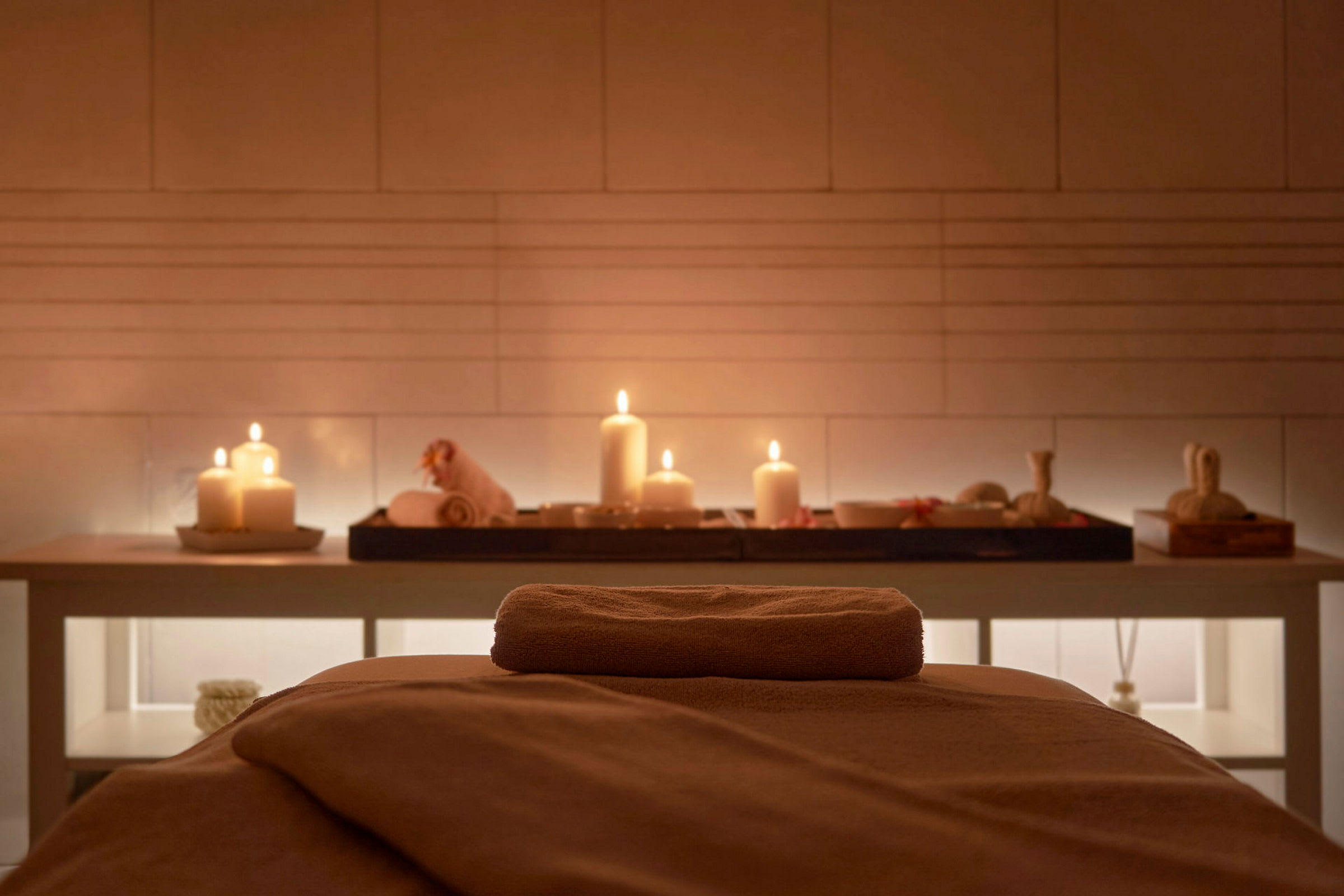 Ett massagebord med en handduk, set i ett spa-område med ljus och dekorativa föremål. (AI-genererad text)