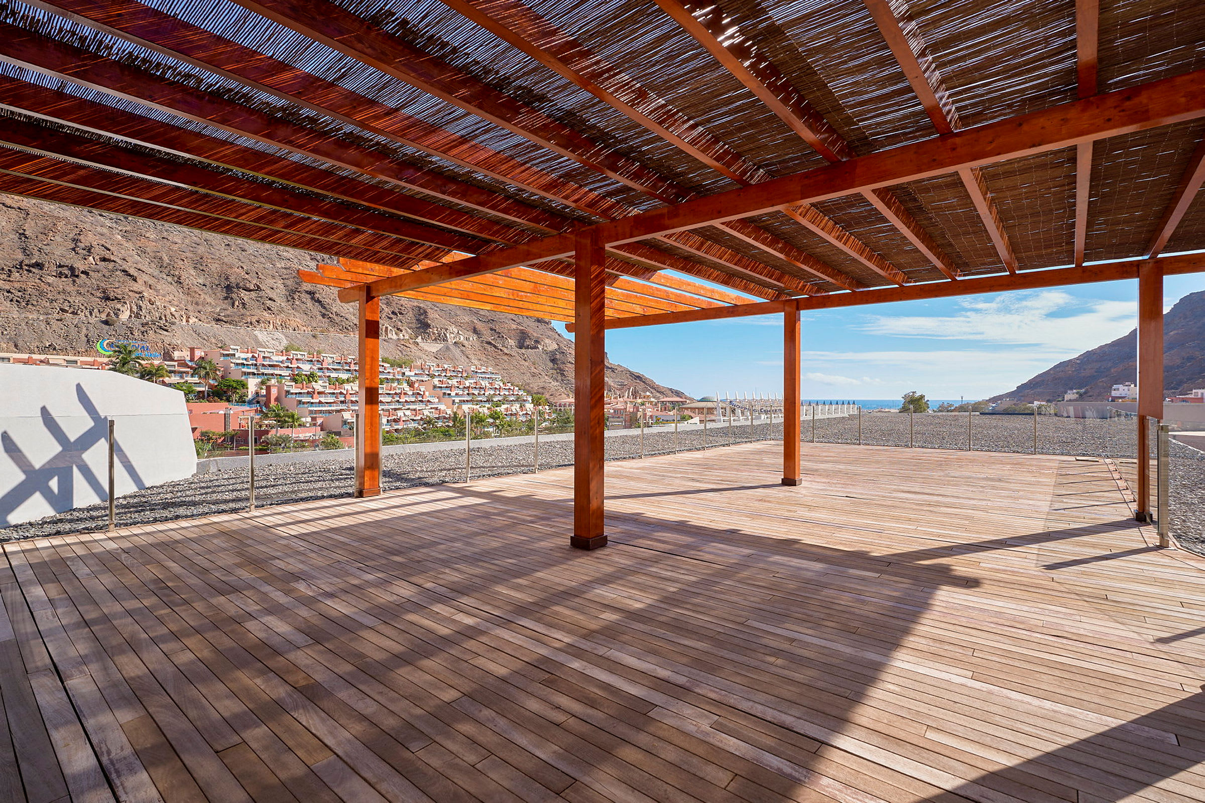 En träpergola med utsikt över en bergssluttning med hus och himlens blå färg i bakgrunden. (AI-genererad text)
