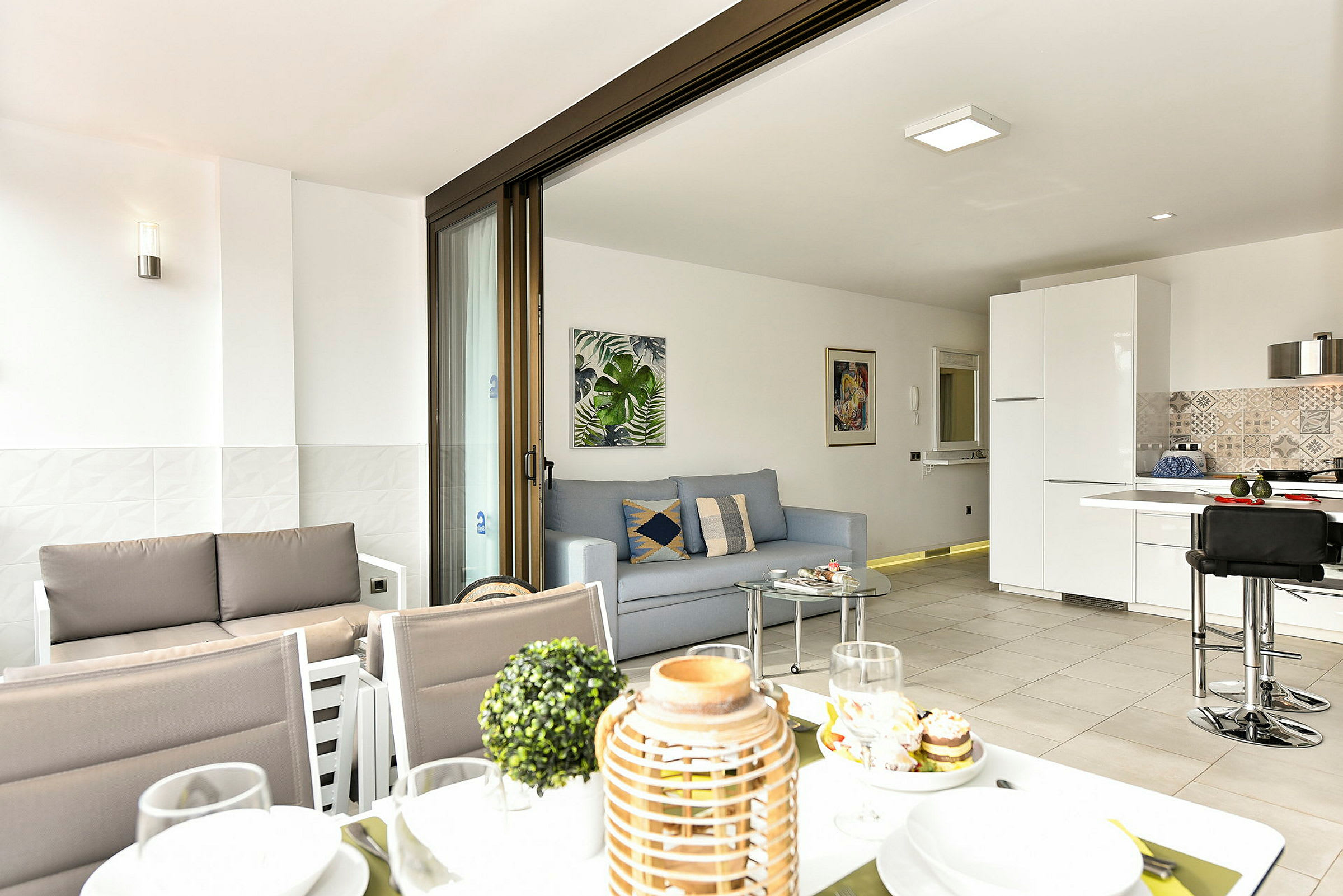 Ett modernt vardagsrum med öppen planlösning och kök, synligt från en terrass med matplats. (AI-genererad text)