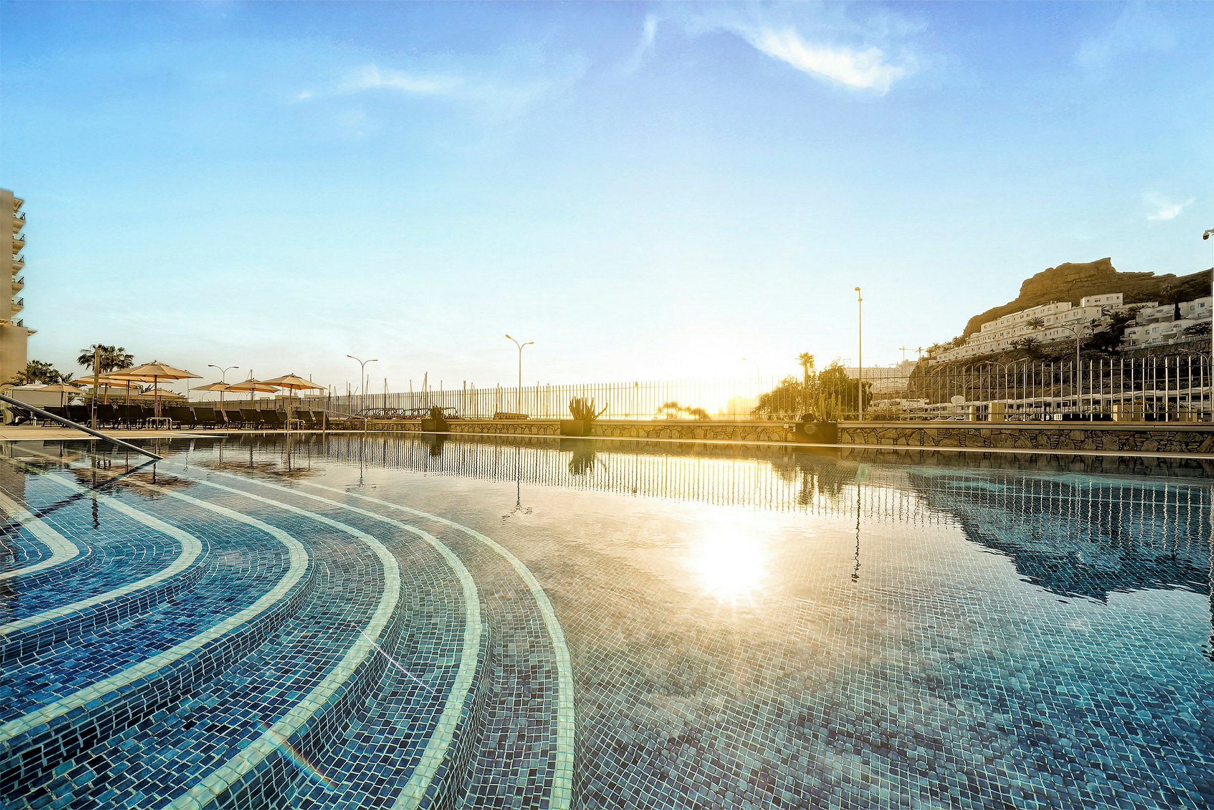 En solnedgång över en pool med trappsteg och omgivande staket. (AI-genererad text)