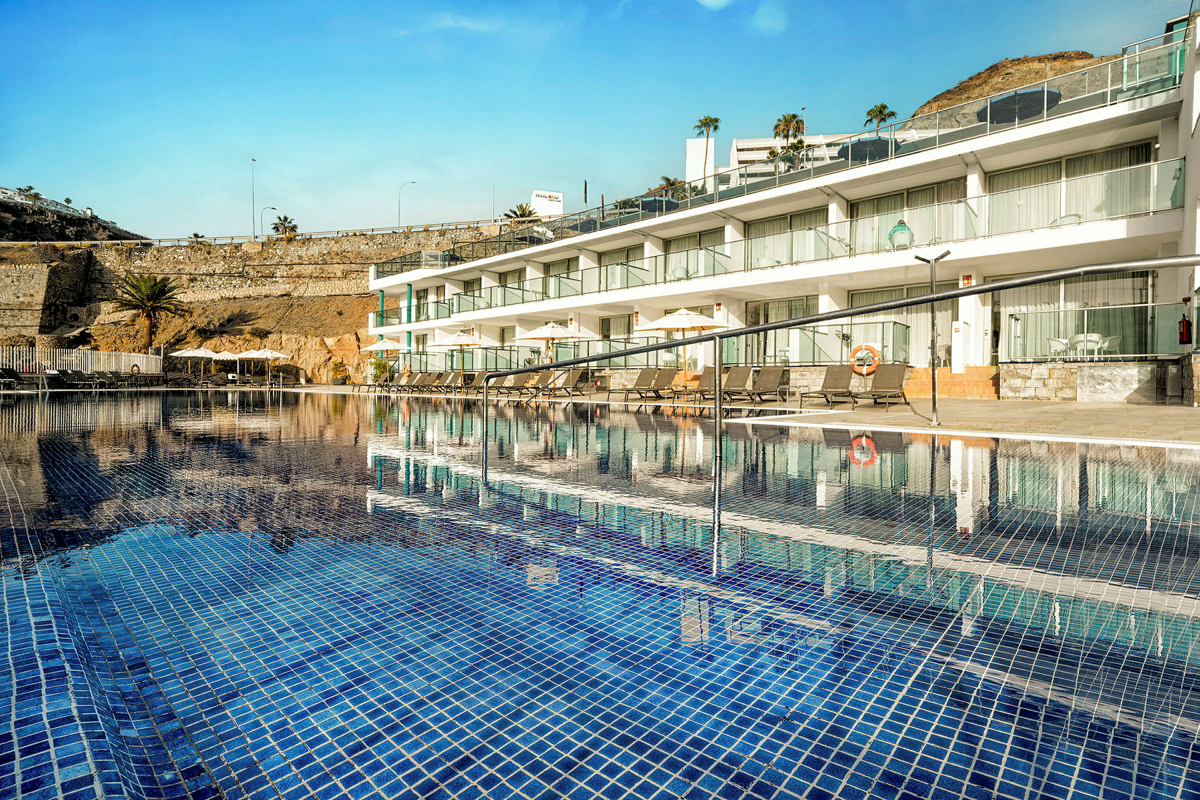 En swimmingpool med blå kakel plattor framför en rad vita hotellrum. (AI-genererad text)