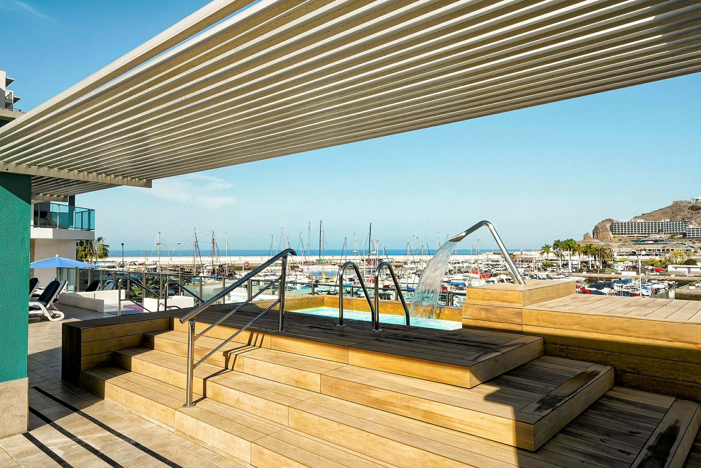 En utsikt över en hamn med båtar, med en pool och sittplatser i förgrunden. (AI-genererad text)