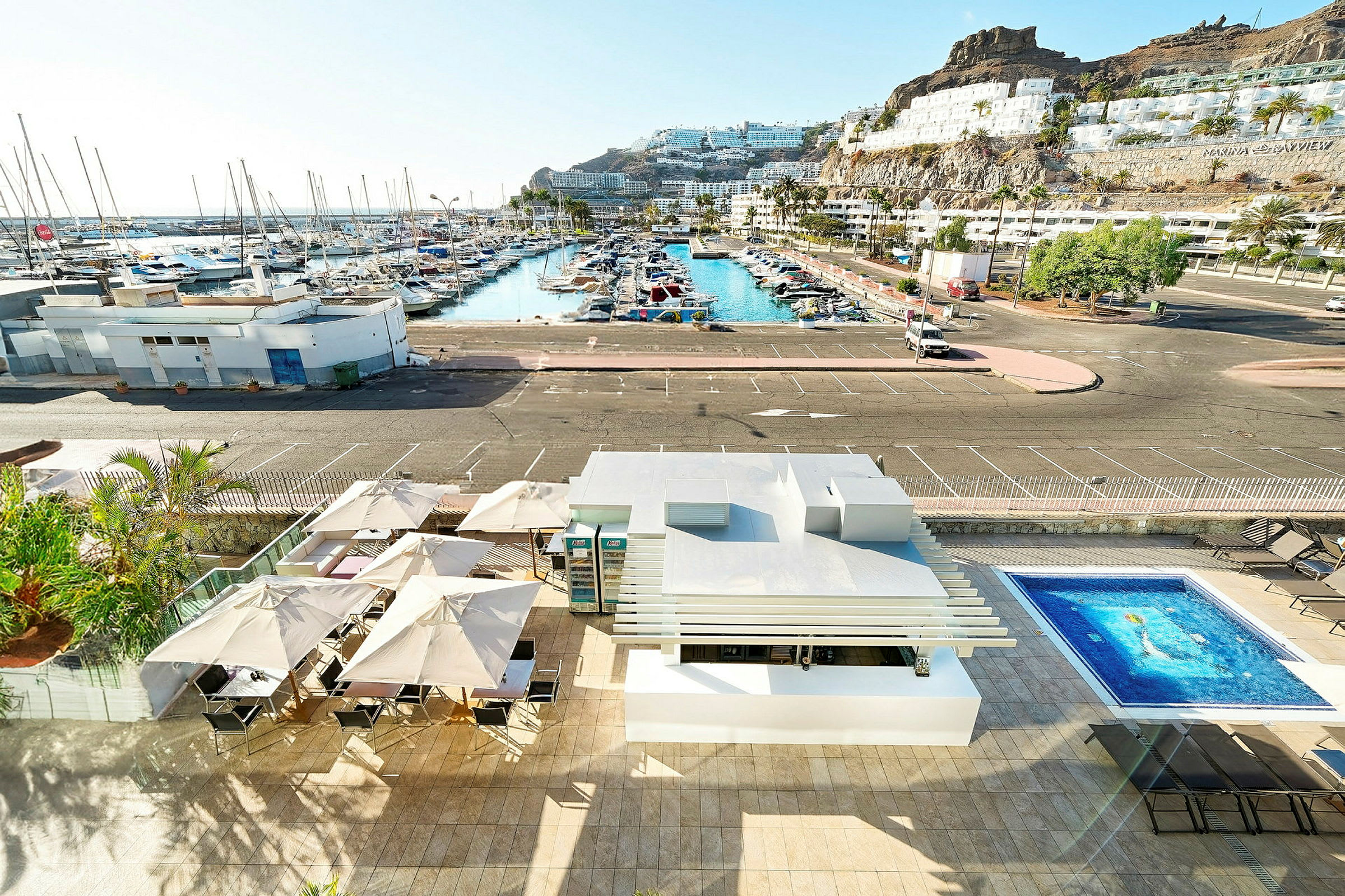 Bild av en sandstrand vid en marina med båtar och semesterboenden på sluttningen. (AI-genererad text)