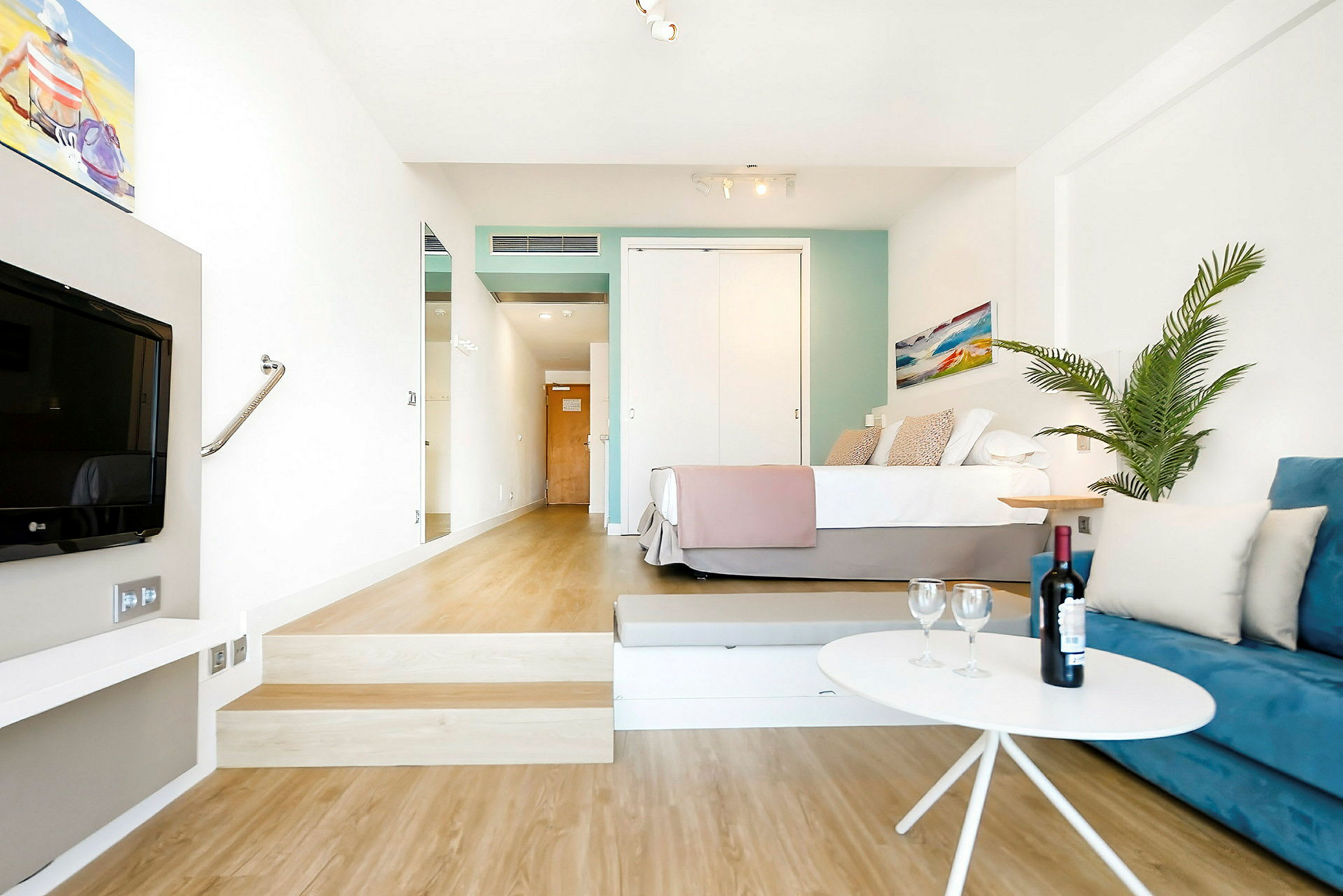 Ett hotellrum med en säng, en blå soffa, ett bord med en vinflaska och glas, och en växt. (AI-genererad text)
