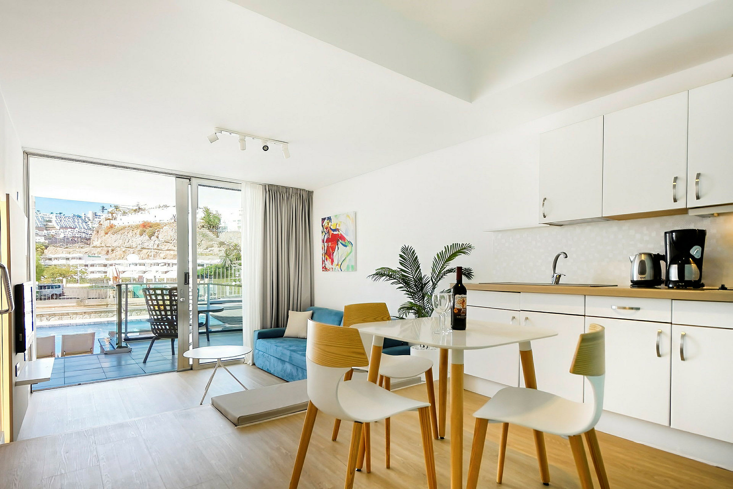Ljust möblerat hotellrum med köksdel och balkong med utsikt. (AI-genererad text)