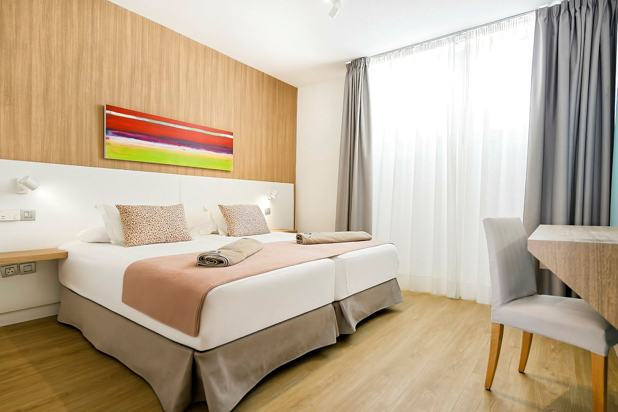 Ett hotellrum med två sängar, en färgglad tavla på väggen, och ett skrivbord med stol. (AI-genererad text)