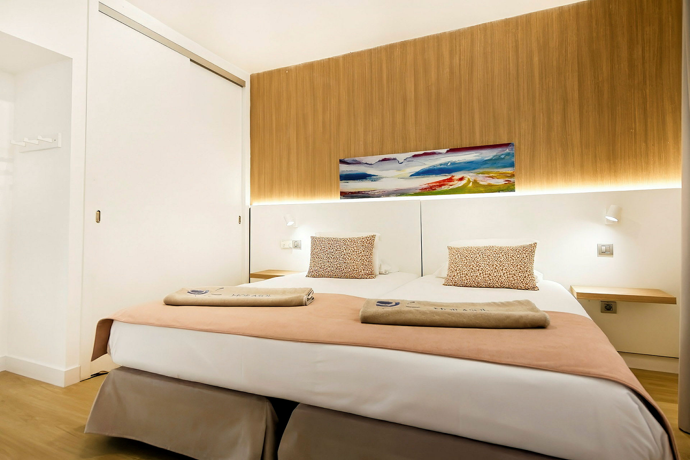 Ett modern hotellrum med två enkelsängar, dekorerade med kuddar och handdukar, en tavla på väggen och träpanel bakgrund. (AI-genererad text)