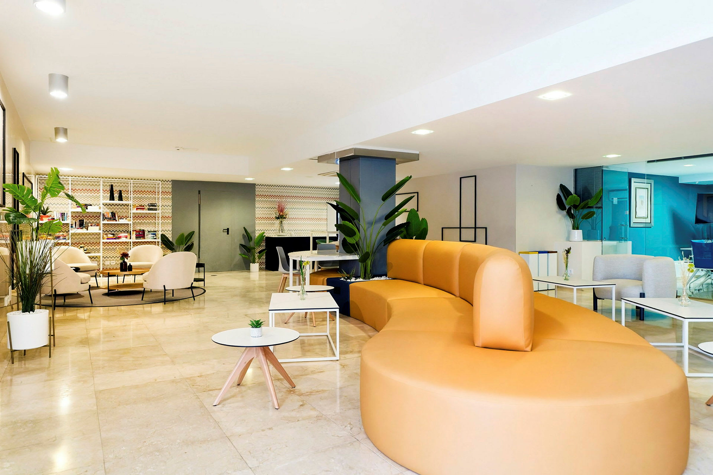 En ljus och modern lounge med en stor gul soffa, bord och grönskande växter. (AI-genererad text)