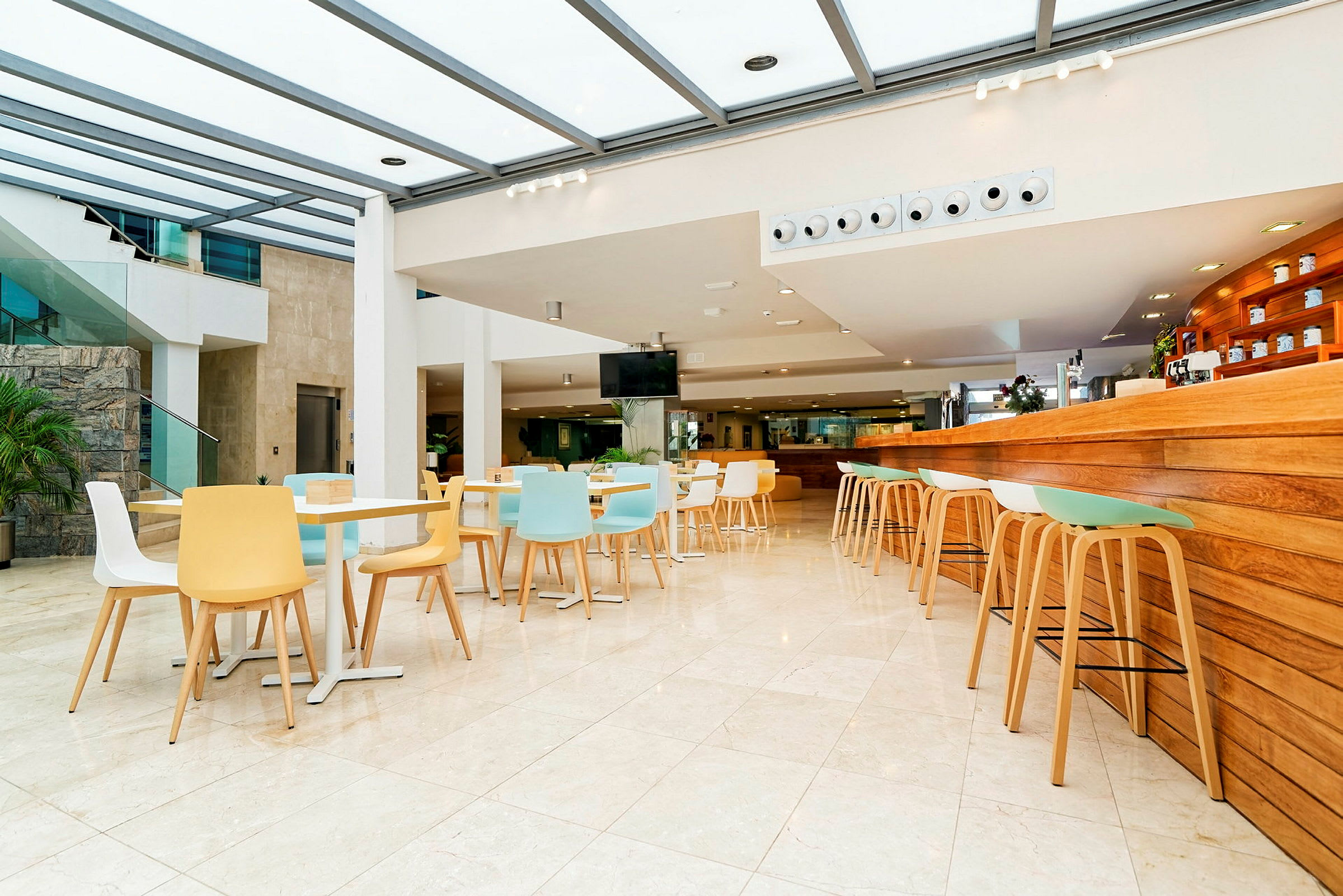 Ljust och modernt kafé med färgglada stolar och ett träpanelat serveringsområde. (AI-genererad text)