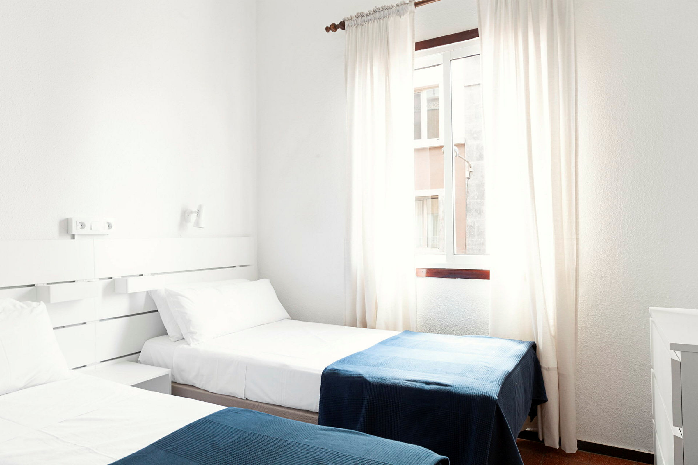 Ett hotellrum med två enkelsängar klädda i vita lakan och blå filtar. (AI-genererad text)