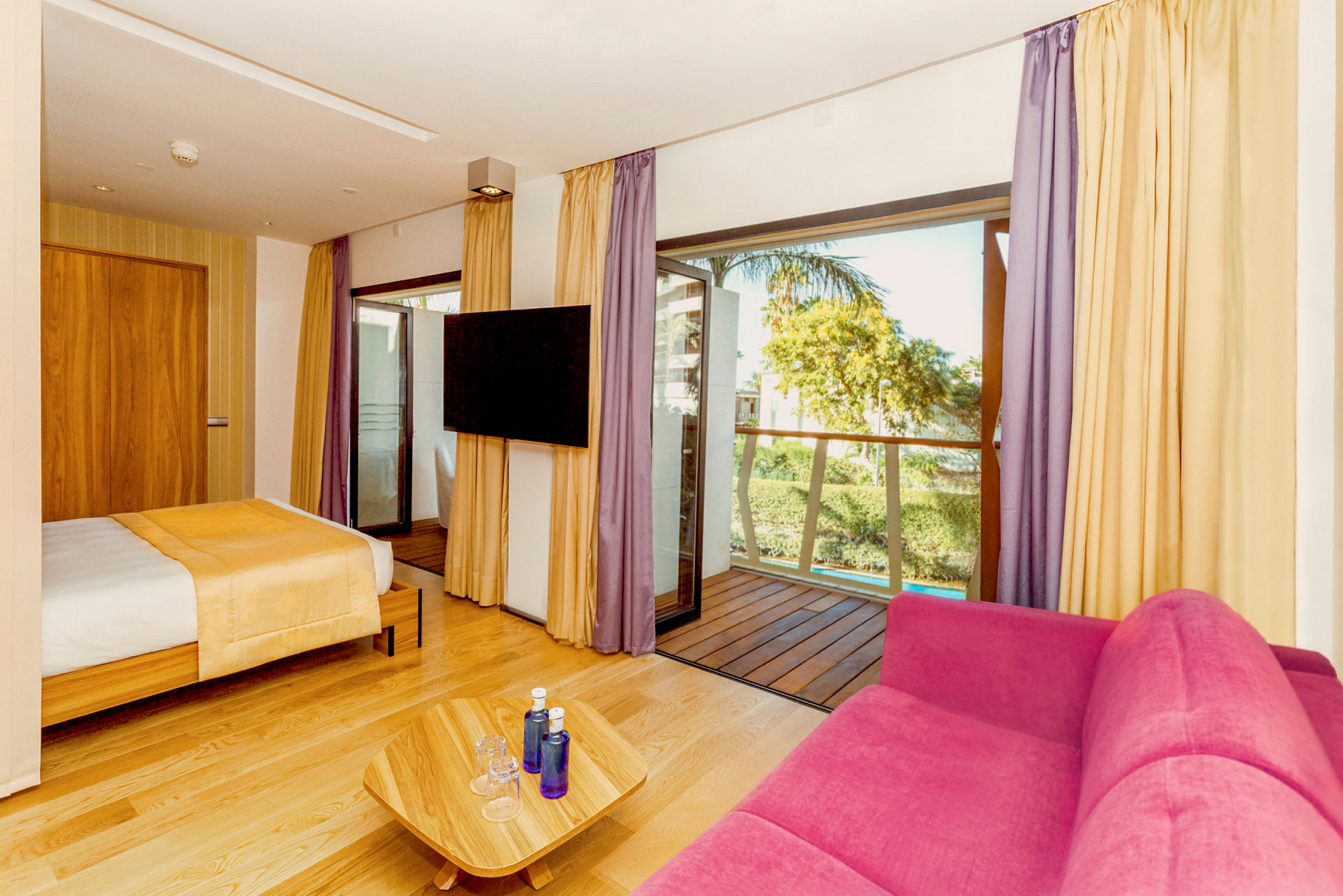 Hotellrum med säng, rosa soffa, TV och balkong. (AI-genererad text)
