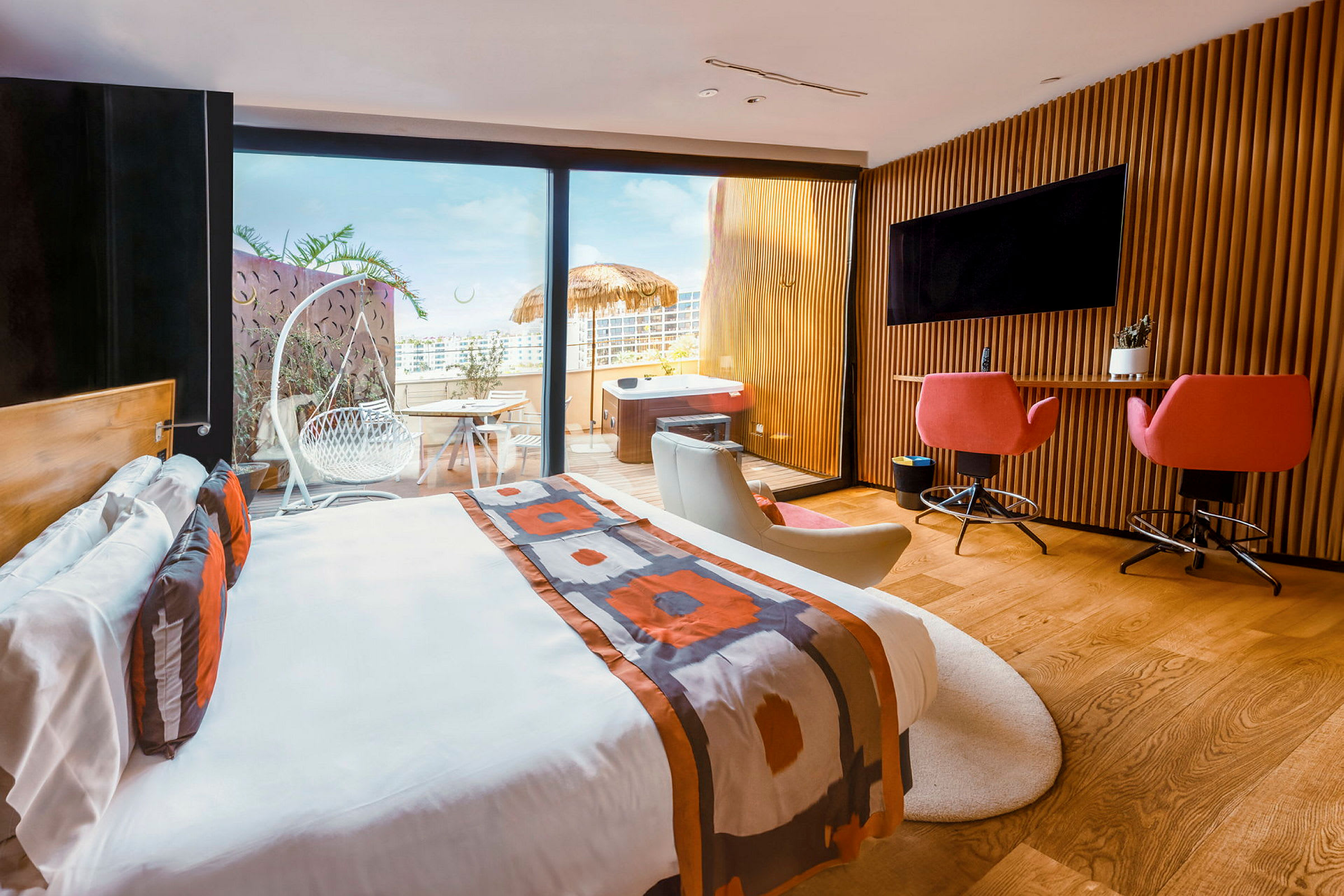 Modernt hotellrum med dubbelsäng, skrivbord, sittmöbler och utgång till en terrass med utemöbler och jacuzzi. (AI-genererad text)