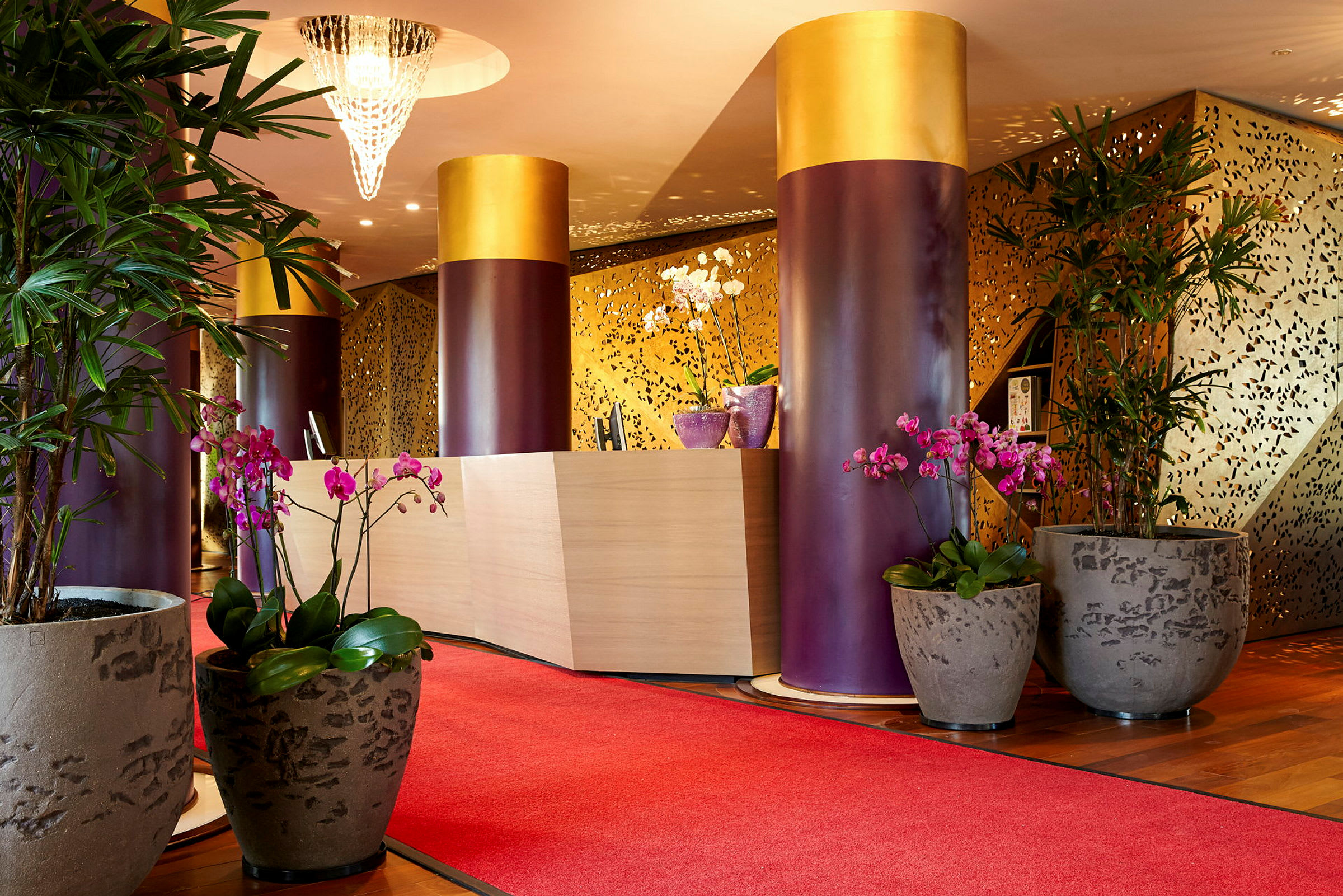 Receptionen på ett elegant hotell med röda mattor, stora krukväxter och dekorativa pelare. (AI-genererad text)