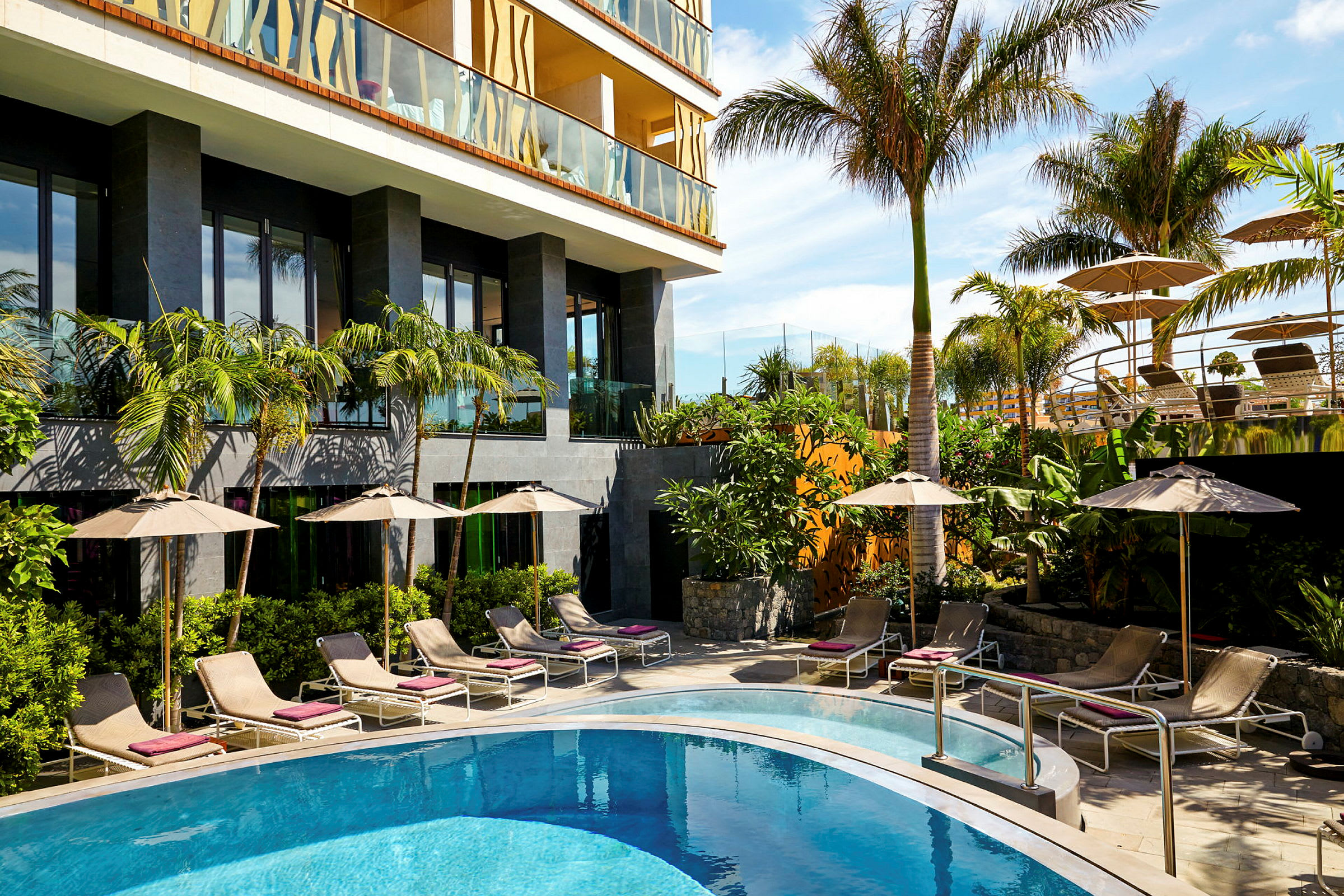 Ett hotell med en pool, solstolar och palmer. (AI-genererad text)