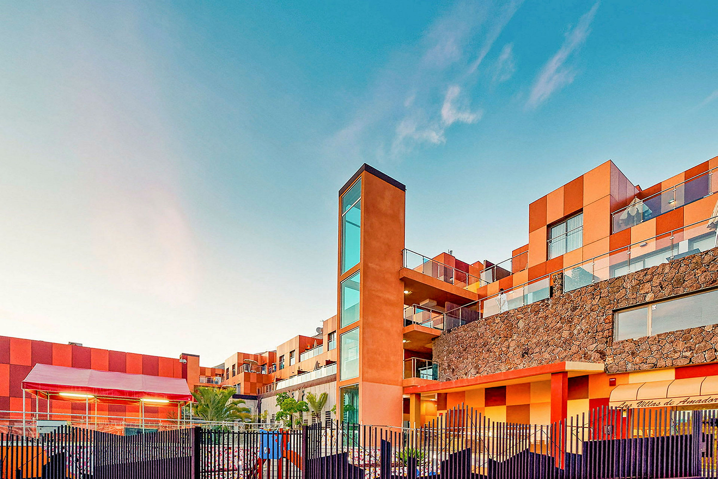 En byggnad med modern arkitektur och varma färger mot en klarblå himmel. (AI-genererad text)