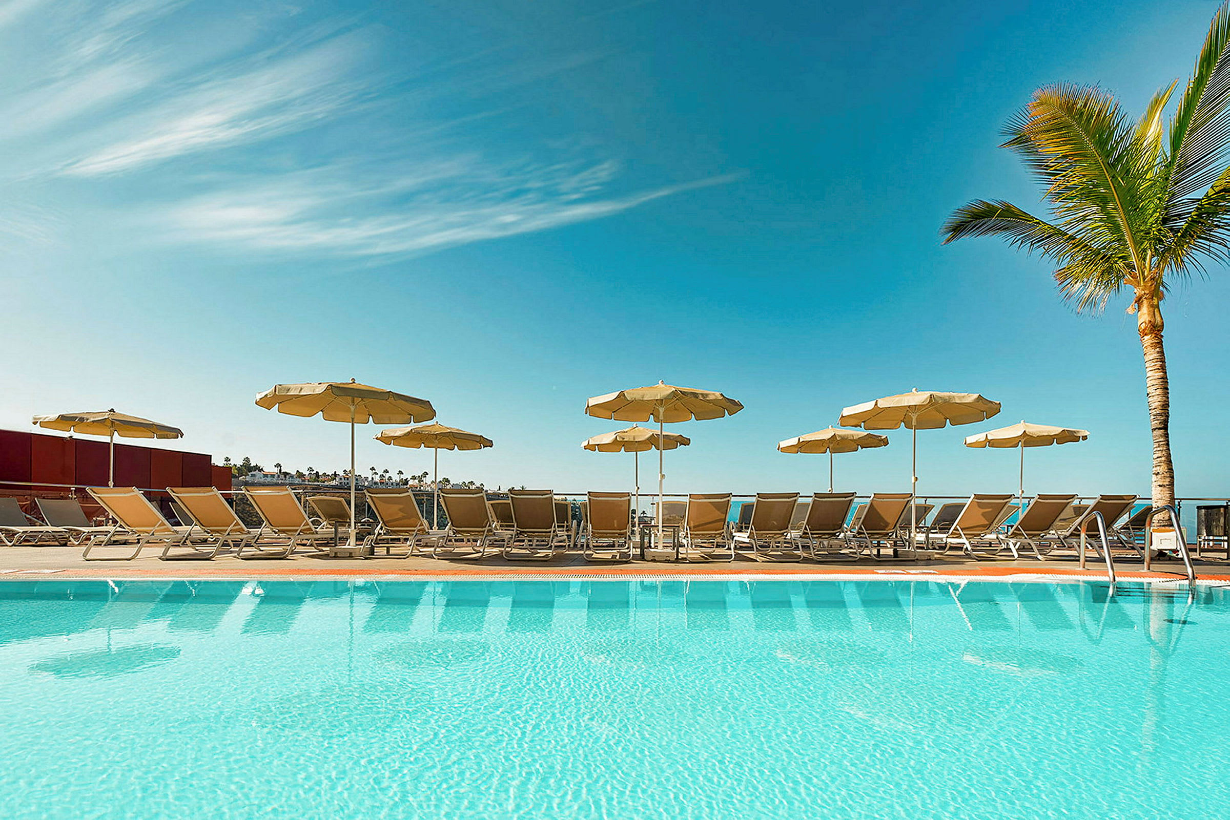 En pool med solstolar och parasoller under en klar blå himmel. (AI-genererad text)