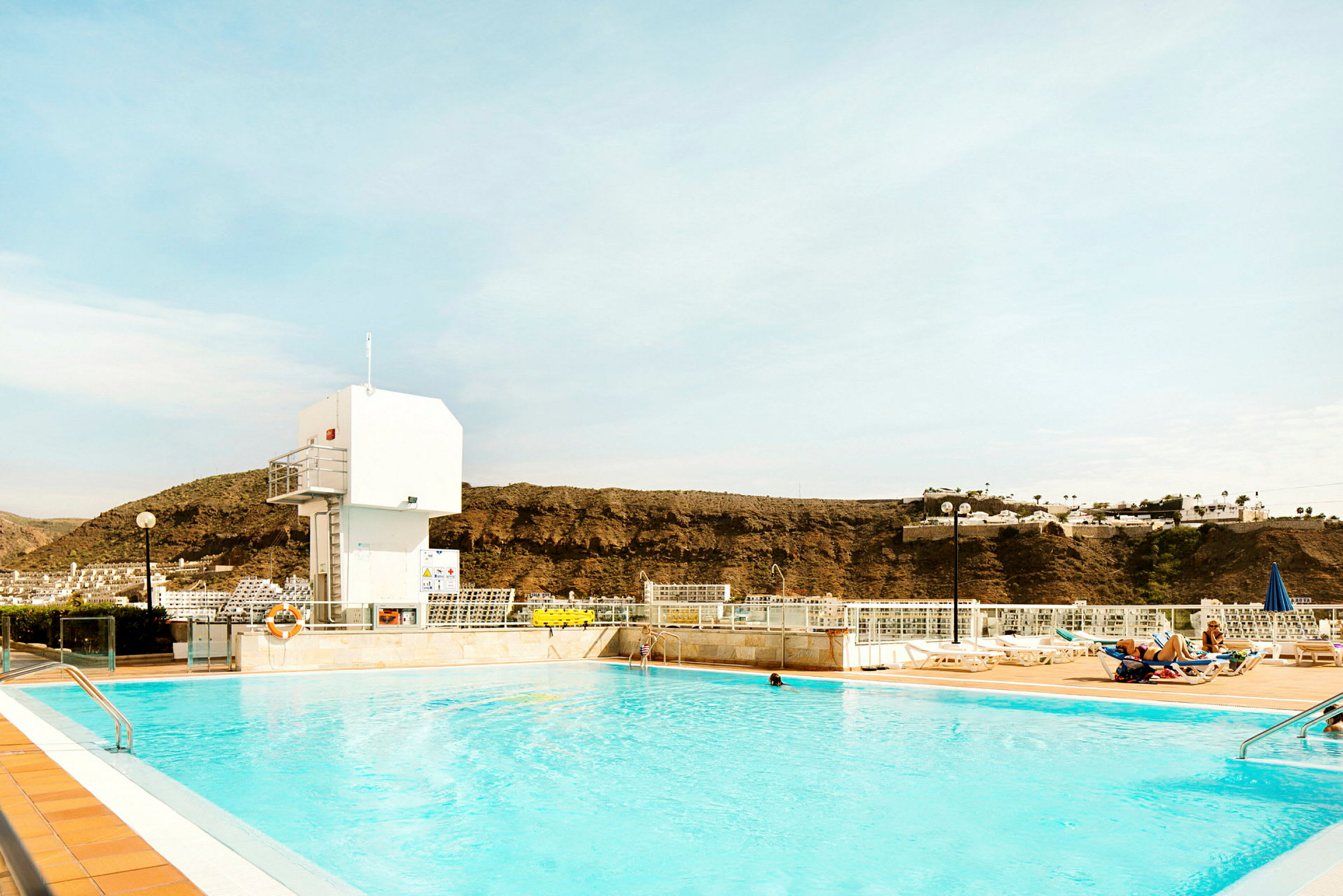 Utomhuspool med solstolar i bakgrunden och berg i fjärran. (AI-genererad text)