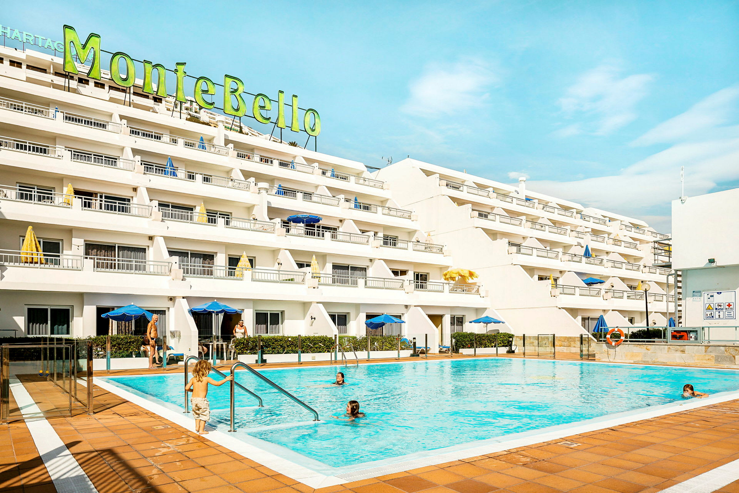 Ett hotell med vita fasader och en utomhuspool framför. (AI-genererad text)