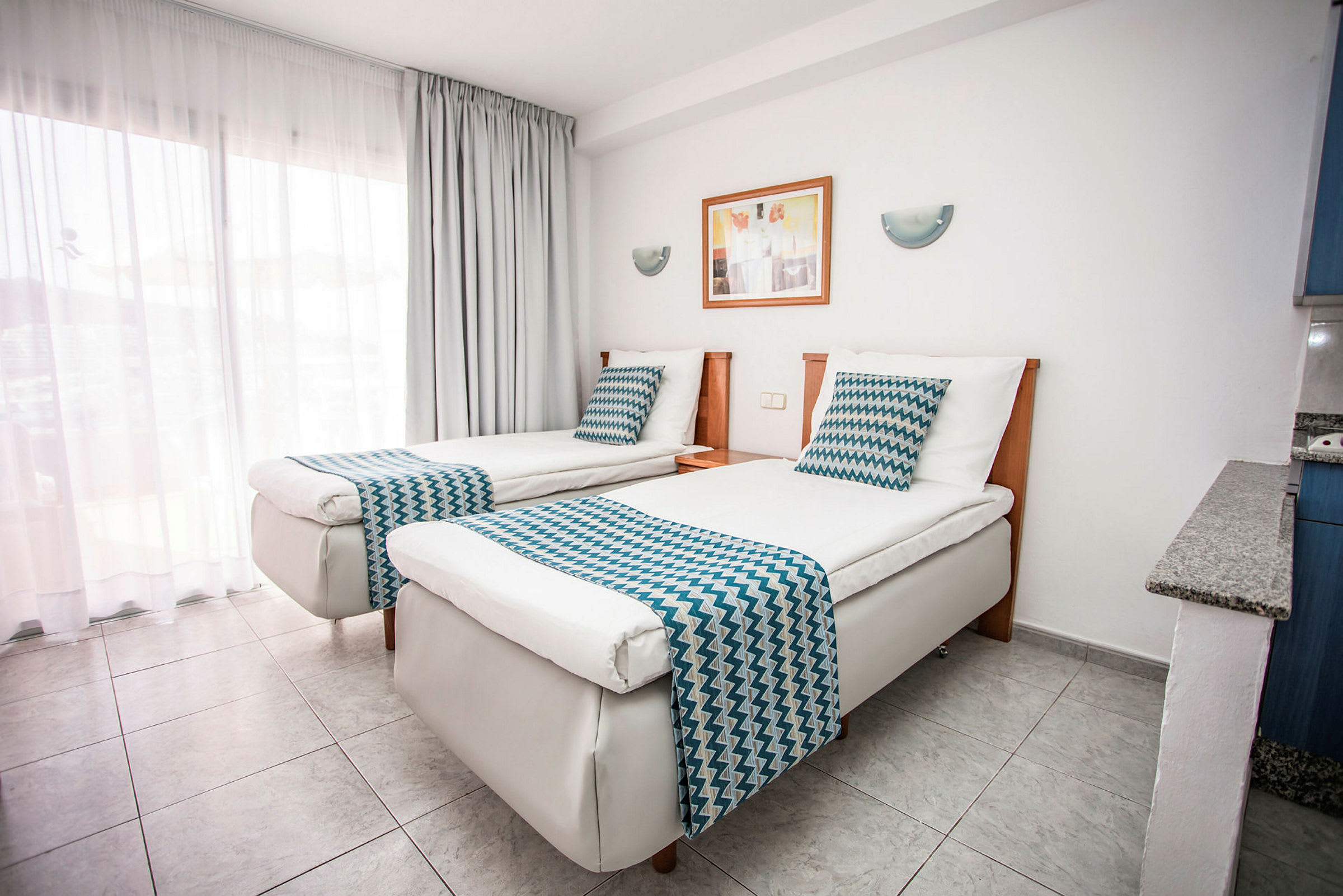 Ett hotellrum med två enkelsängar, vit sängklädsel och blåmönstrade överkast. (AI-genererad text)