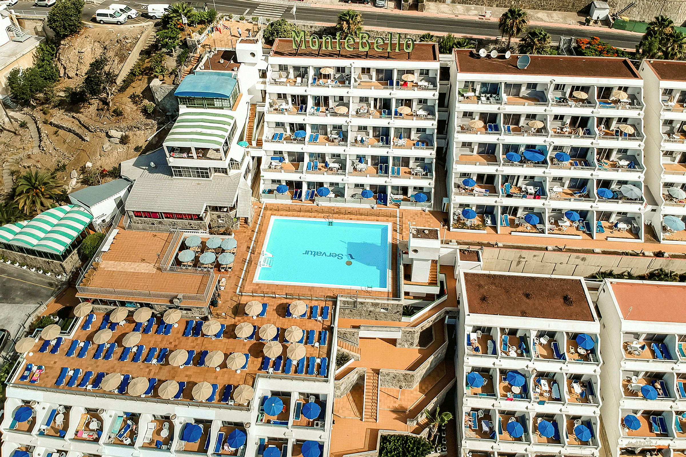 Flygvy över hotell Montebello med pool och solstolar. (AI-genererad text)