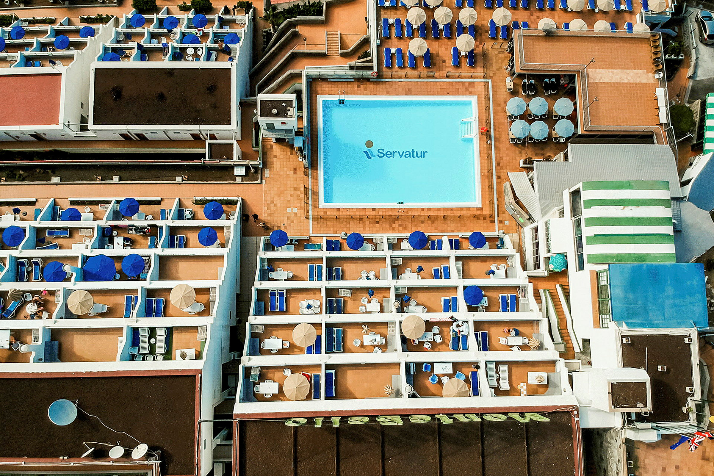 Flygfoto över hotellområde med pool och terrasser. (AI-genererad text)